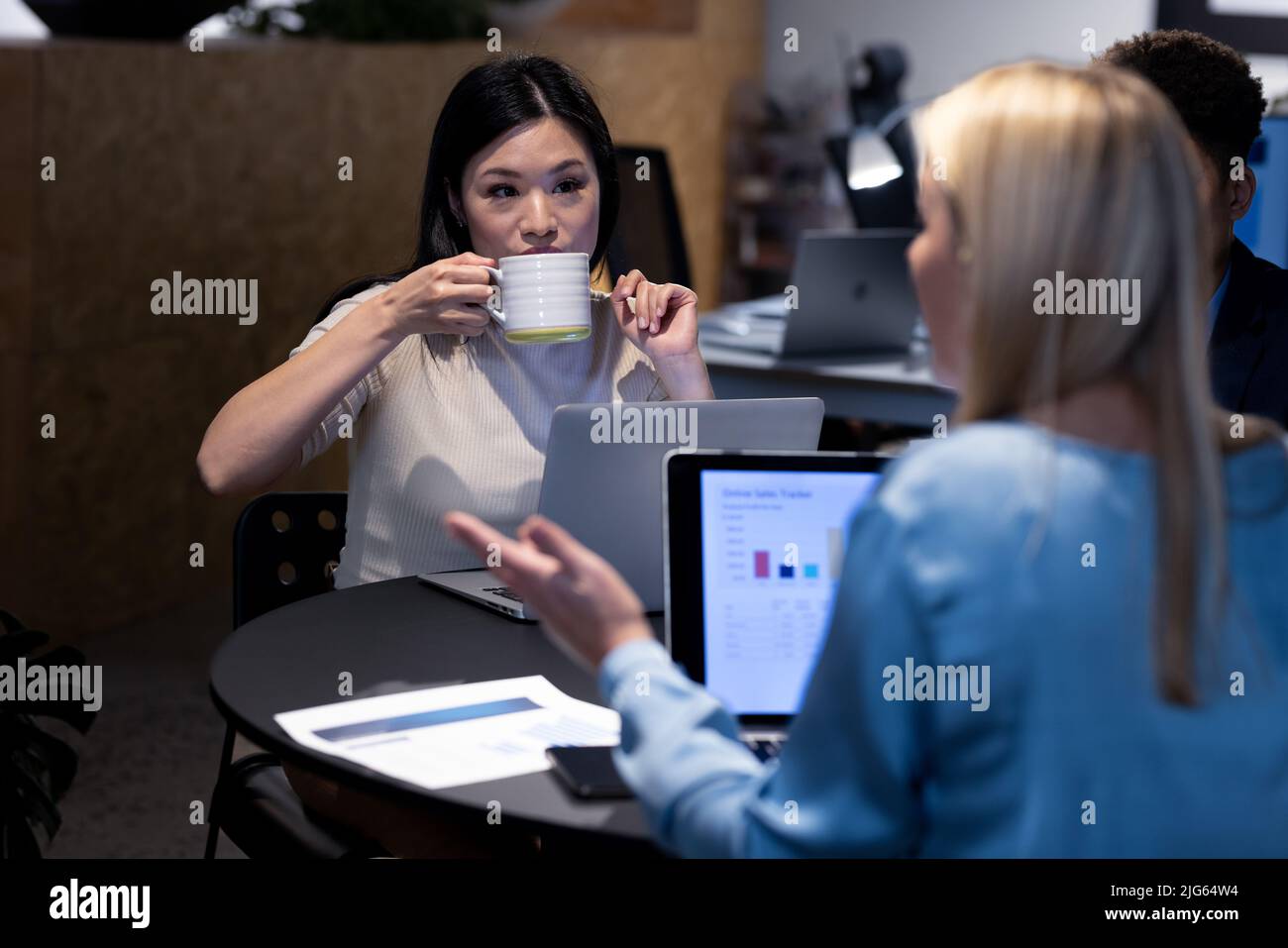 Asiatische Geschäftsfrau trinkt Kaffee, während sie spät mit einem kaukasischen Kollegen im Büro in der Nacht arbeitet Stockfoto