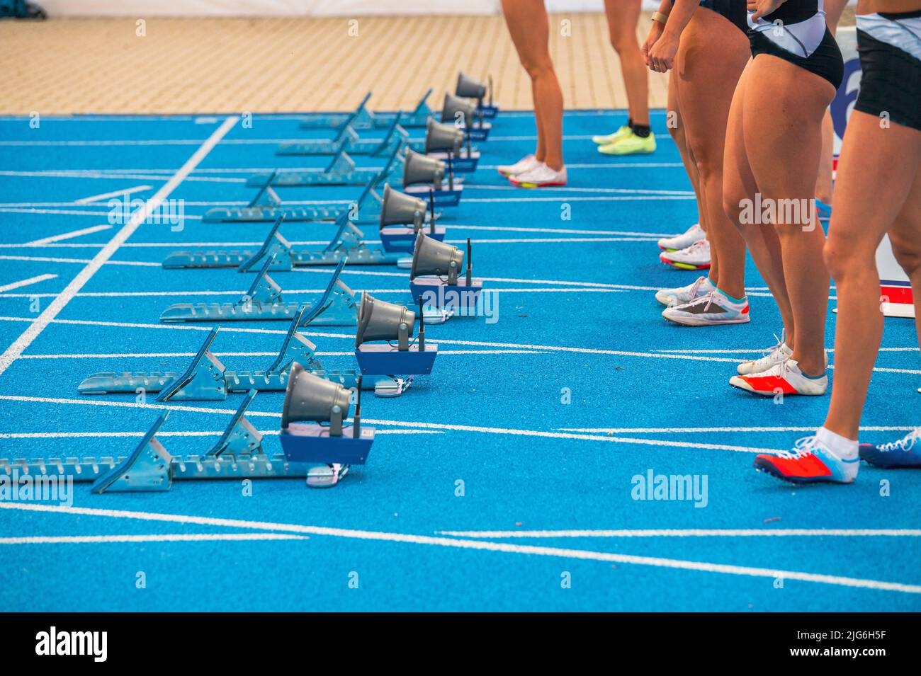 Leichtathletik, Laufen und Sprinten. Beine von Profisportlern vor dem Start eines Sprint-Rennens. Weibliche Athleten stehen vor der blauen Piste Stockfoto