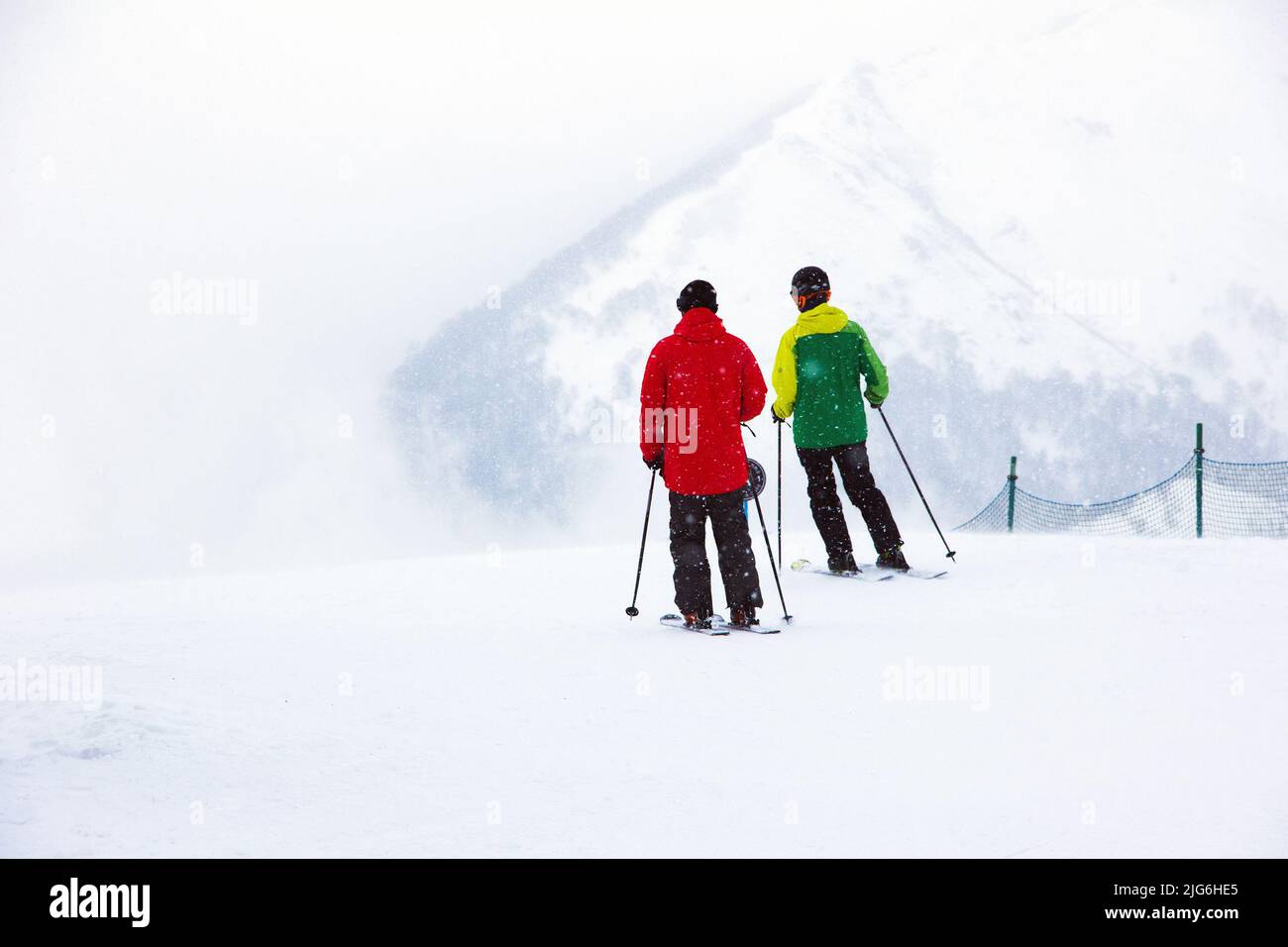 Zwei Skifahrer in roten und blauen Skianzügen, bevor sie vor dem Hintergrund von weißem Schnee und Berggipfeln in der Ferne, Bakuria, einen Berghang hinunterfahren Stockfoto