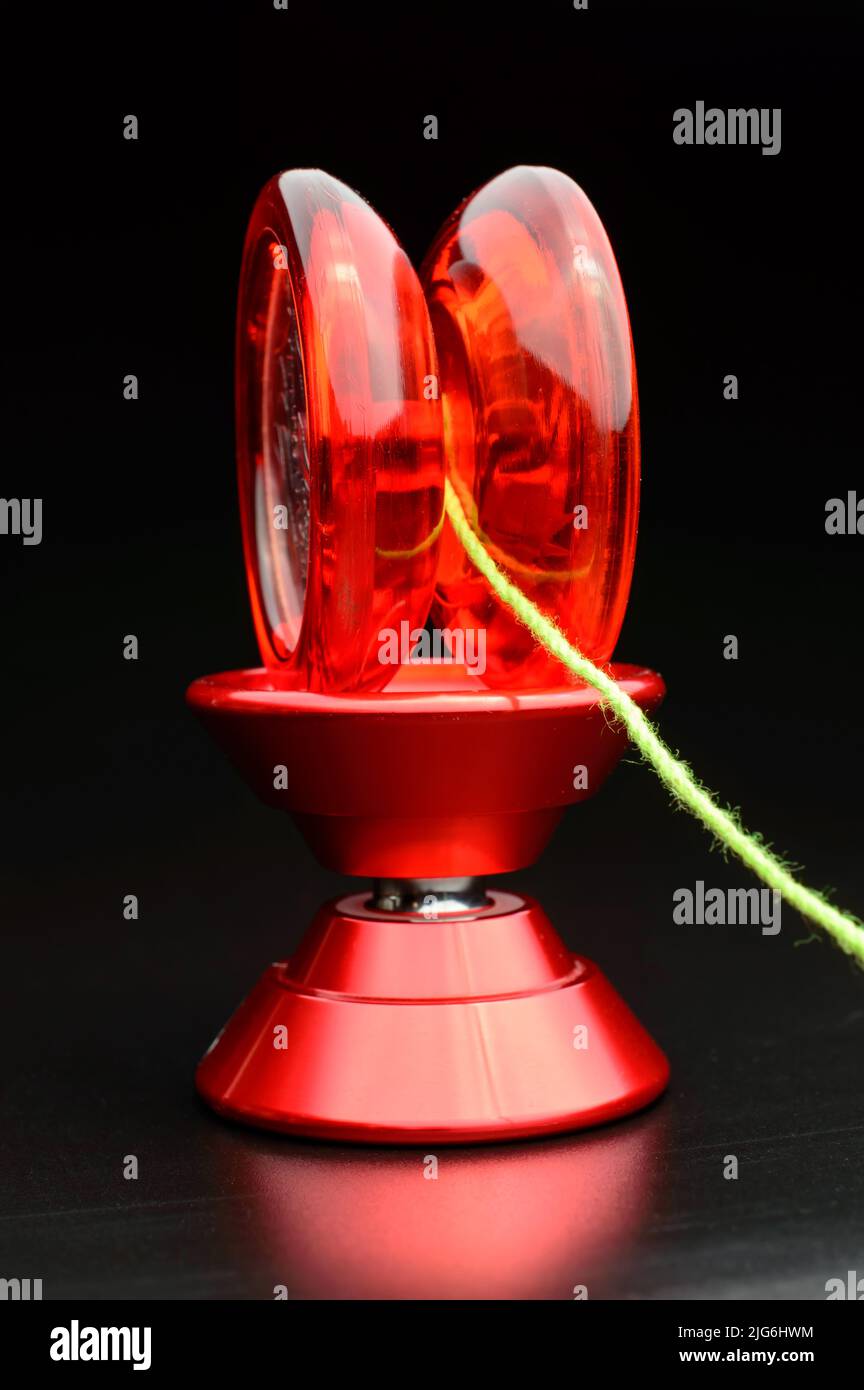 Rotes Kunststoff-Yo-Yo-Spielzeug auf der Oberseite eines anderen Aluminium-Yo-Yo isoliert auf dunklem Hintergrund mit einem hübschen grünen Seil daran befestigt. Stockfoto