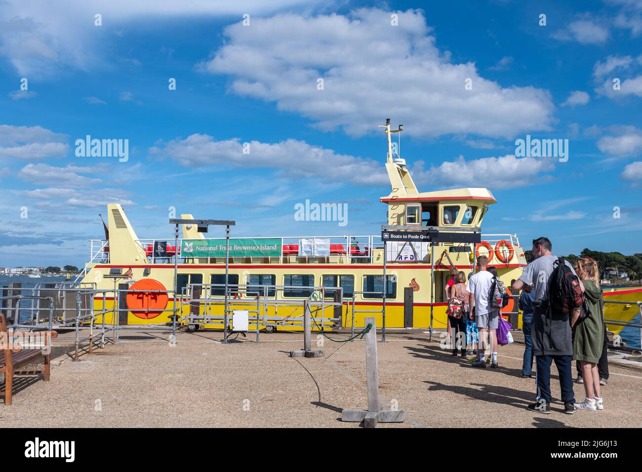 Gelbes Boot vor dem Brownsea Island Quay, um Passagiere für die Rückfahrt nach Poole, Dorset, England, Großbritannien, an einem sonnigen Sommertag abzuholen Stockfoto