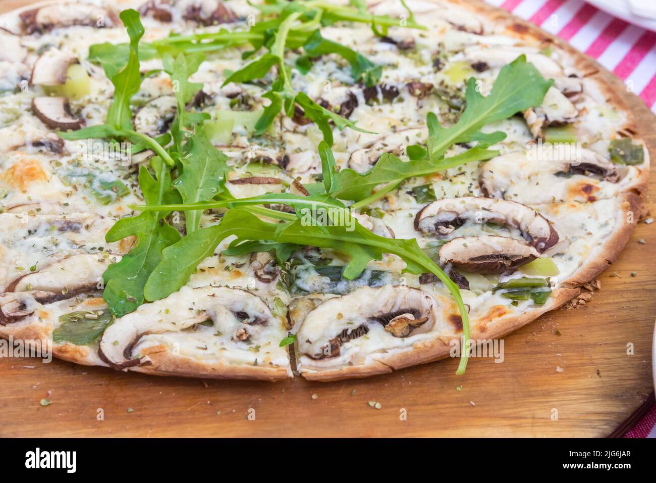 Traditionelles deutsches Gericht Flammkuchen mit Käse, Pilzen, Kräutern und Rucola Stockfoto