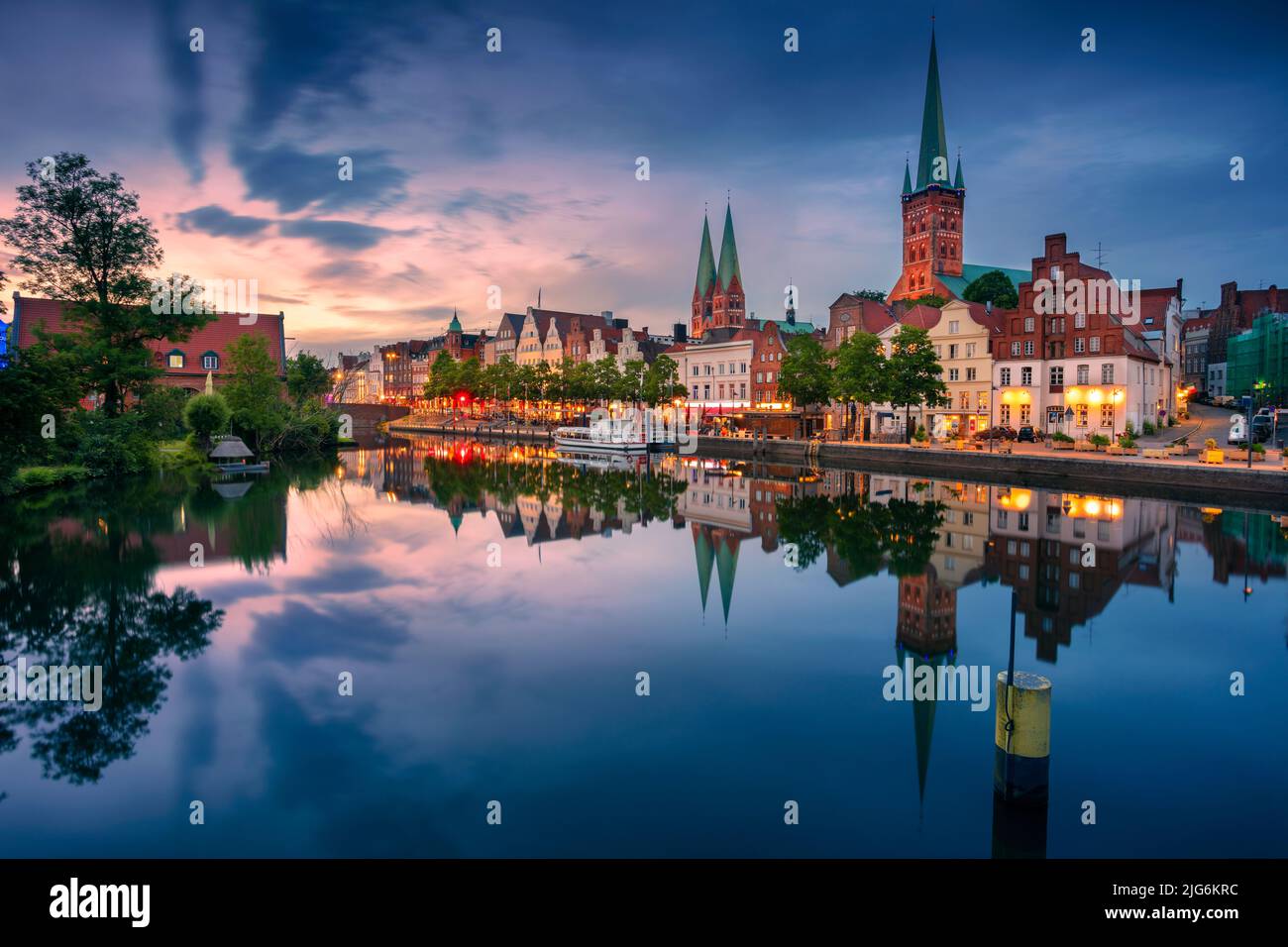 Lübeck, Deutschland. Stadtbild des Lubecker Flussufers mit Spiegelung der Stadt im Trave bei Sonnenuntergang. Stockfoto