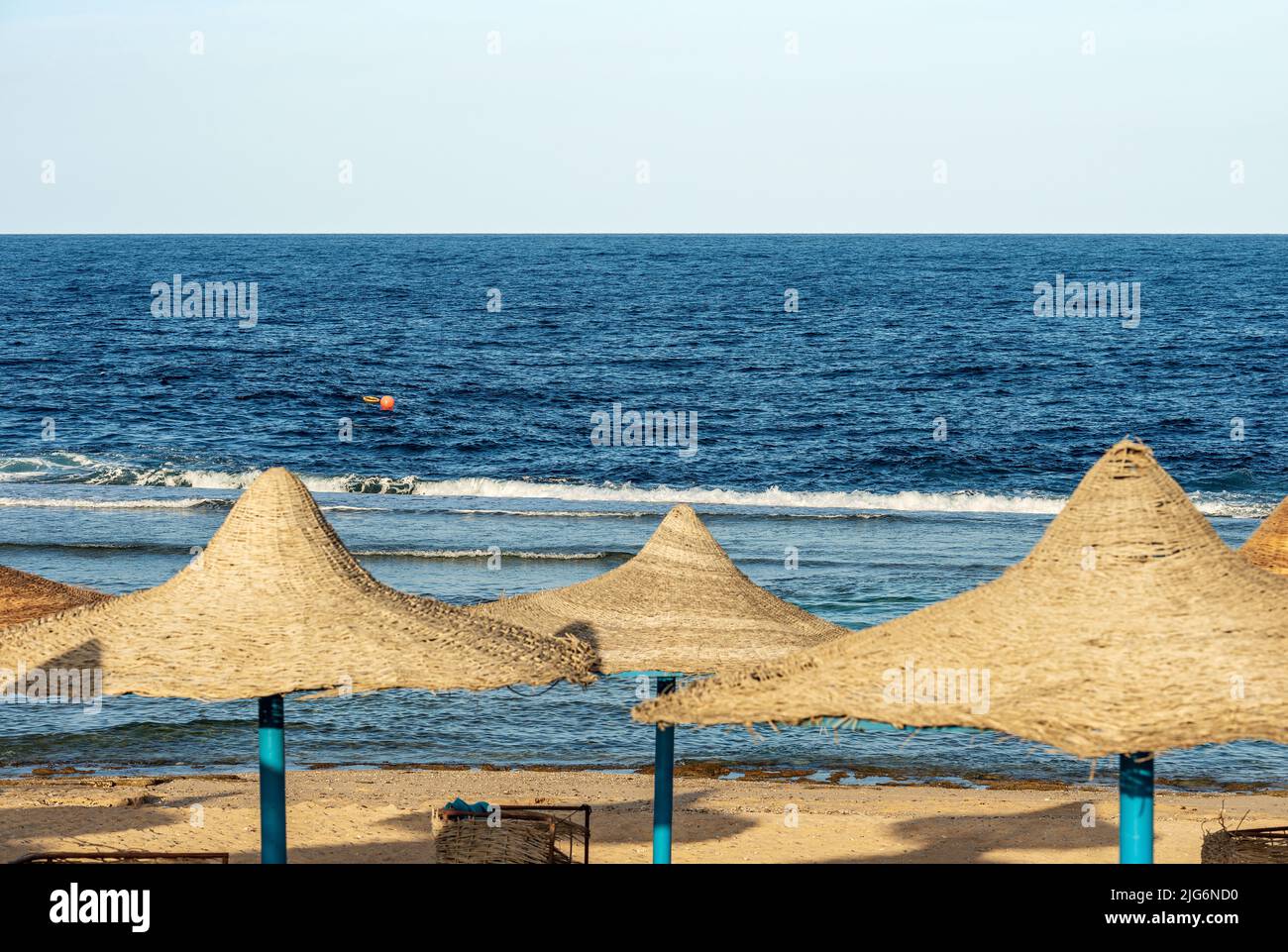 Seascape und Sandstrand mit einer Gruppe von Stroh-Sonnenschirmen an der Küste des Roten Meeres mit Wellen brechen auf dem Korallenriff, in der Nähe von Marsa Alam, Ägypten. Stockfoto