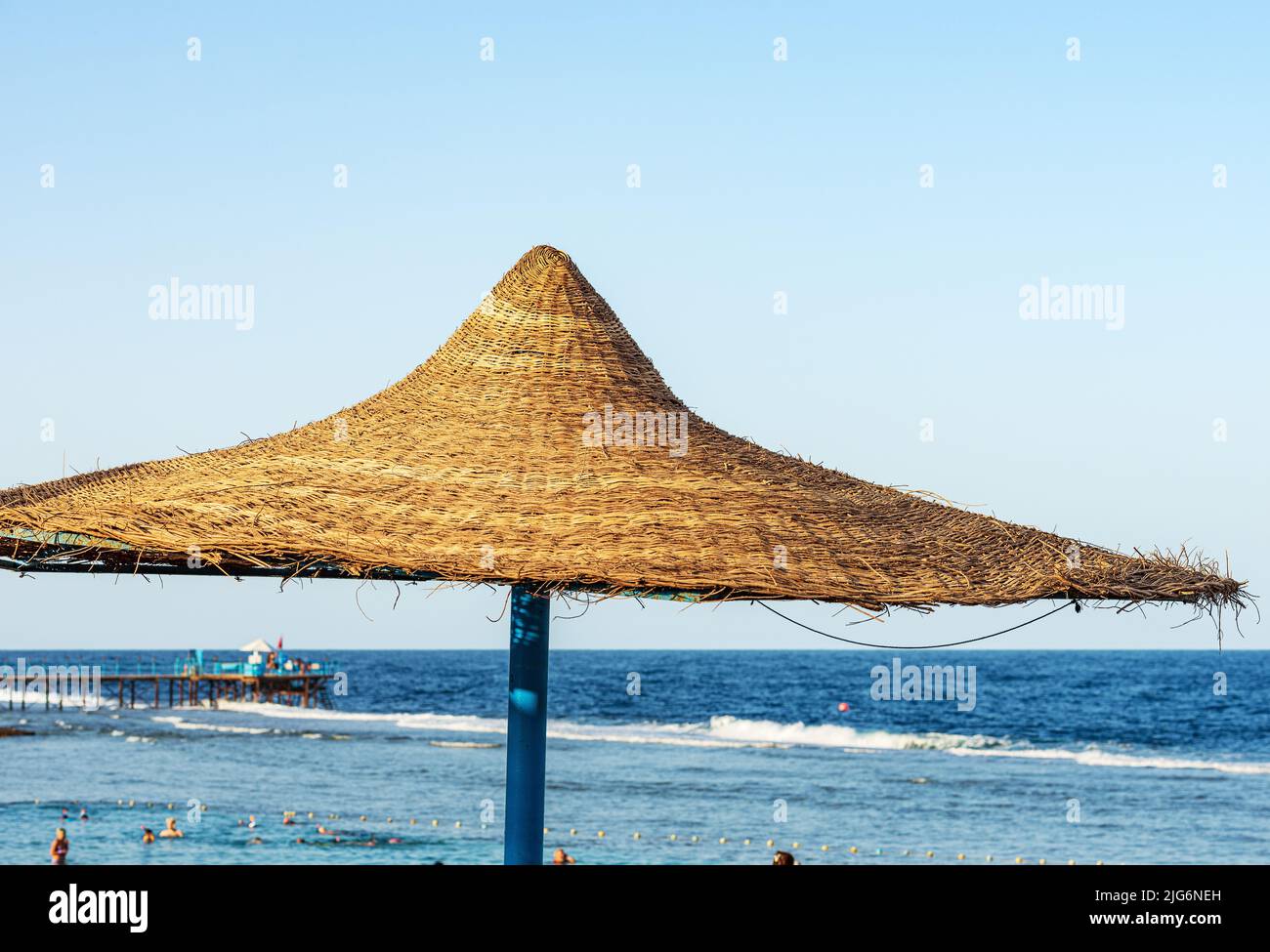 Stroh-Sonnenschirm. Strandurlaub an der Küste des Roten Meeres in der Nähe von Marsa Alam, Sahara Wüste, Ägypten, Nordafrika. Pier über dem Korallenriff. Stockfoto