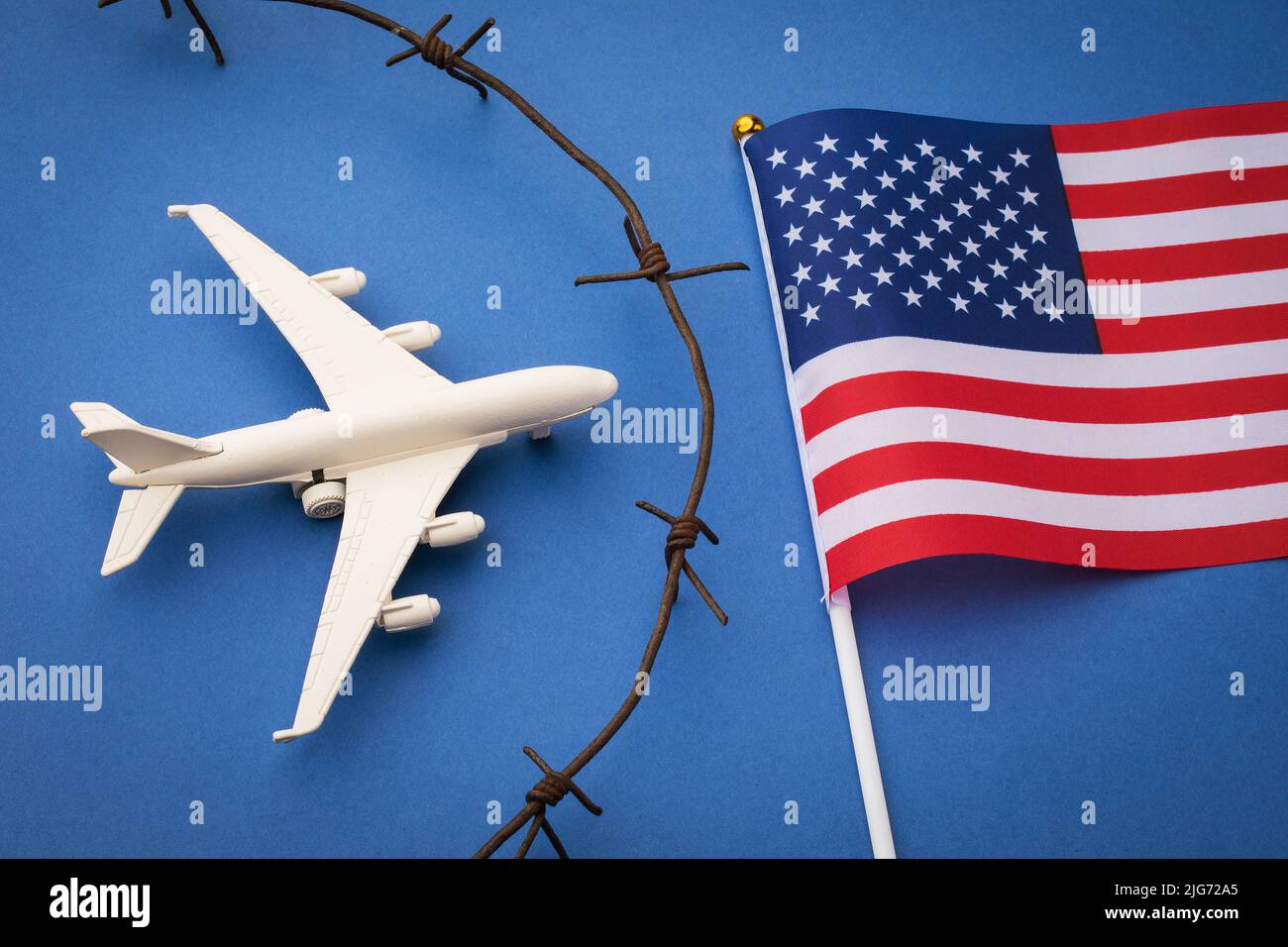 USA geschlossenes Luftraumkonzept, Spielzeugflugzeug, Stacheldraht und Flagge auf blauem Hintergrund Stockfoto