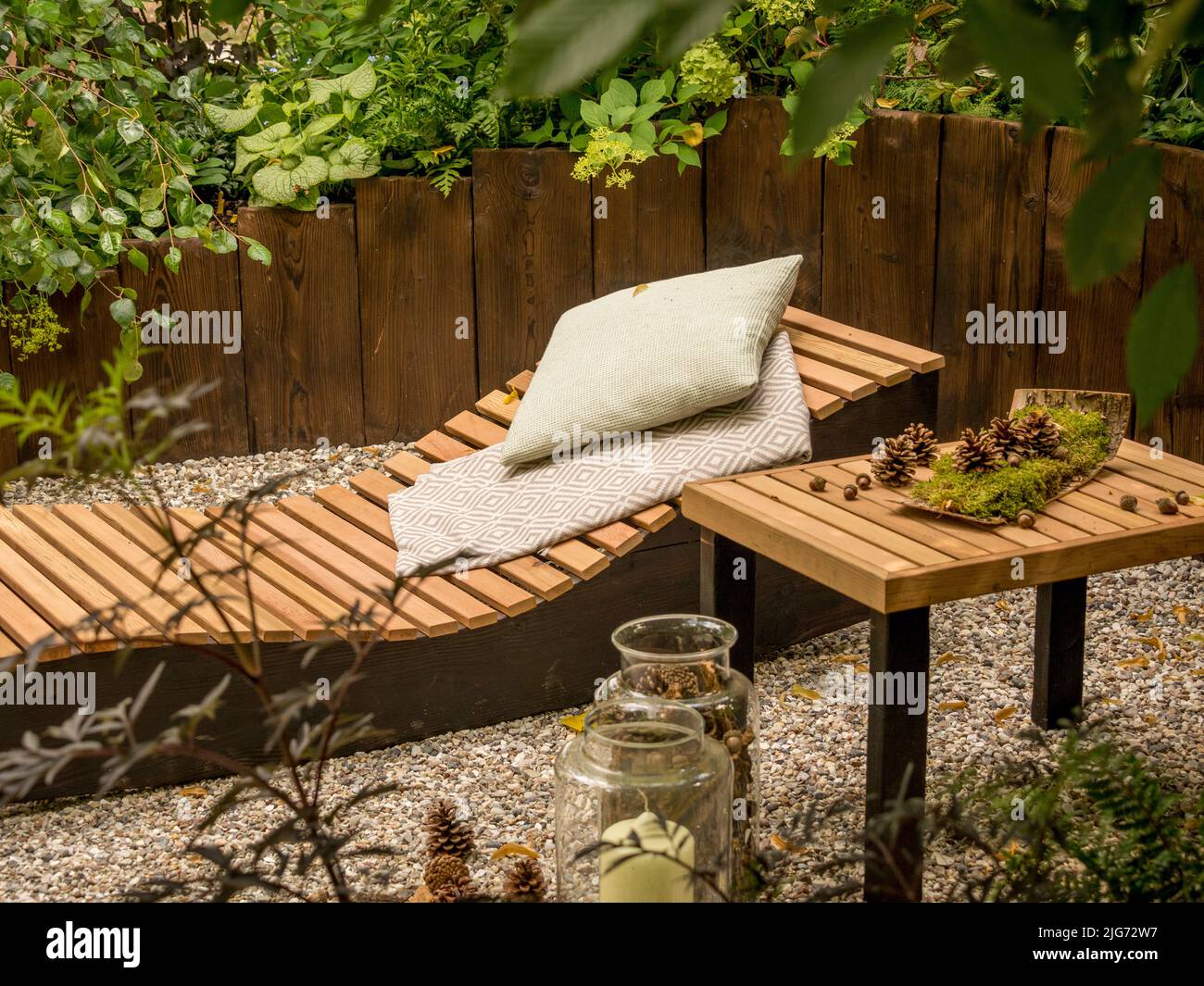Hölzerne Sonnenliege und Tisch im schattigen Bereich des Schaugartens beim Hampton Court Palace Garden Festival in London. Stockfoto