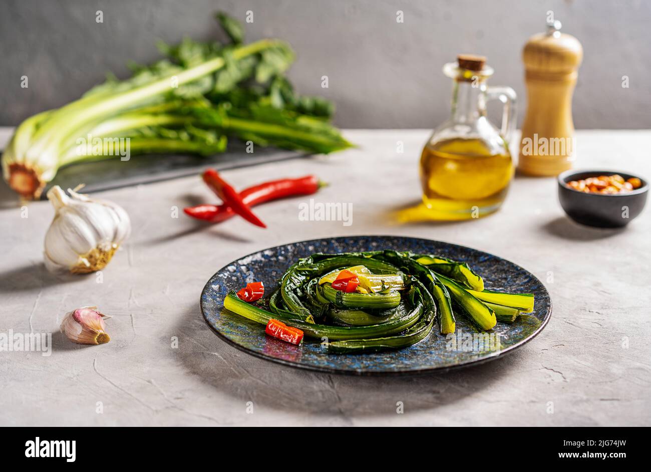 Zichorien-Grüns mit Knoblauch und heißem rotem Papier auf blauem Teller mit Zutaten beiseite geschmort. Stockfoto