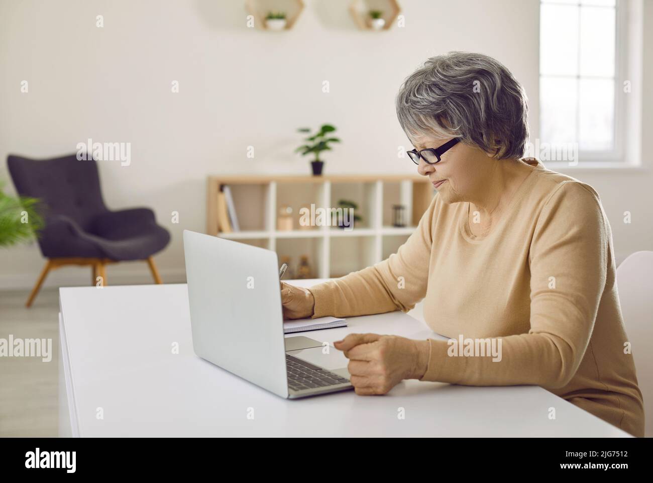 Ältere Frau, die am Schreibtisch sitzt und ihren Laptop für Fernarbeiten oder Lernen nutzt Stockfoto