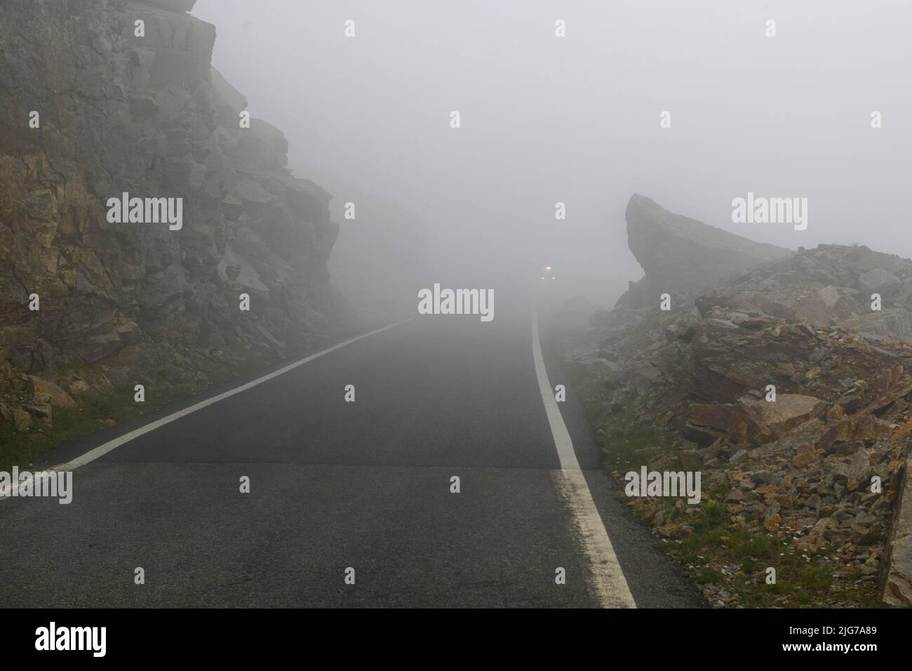 Niedrige Wolken auf kurvigen Bergstraße Pass am Gipfel des Colle del Nivolet, im Hintergrund Licht von entgegenkommenden Fahrzeug, Col du Nivolet, Graian Alps Stockfoto