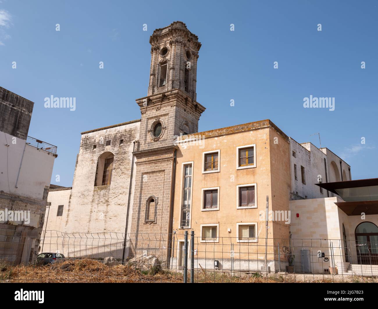 Eine verlassene Kirche mit einer verzierten, aber verdunkelten Fassade, die in der Abenddämmerung von Straßenlaternen in den Hinterstraßen von Nardo, Apulien, reflektiert wird. Stockfoto