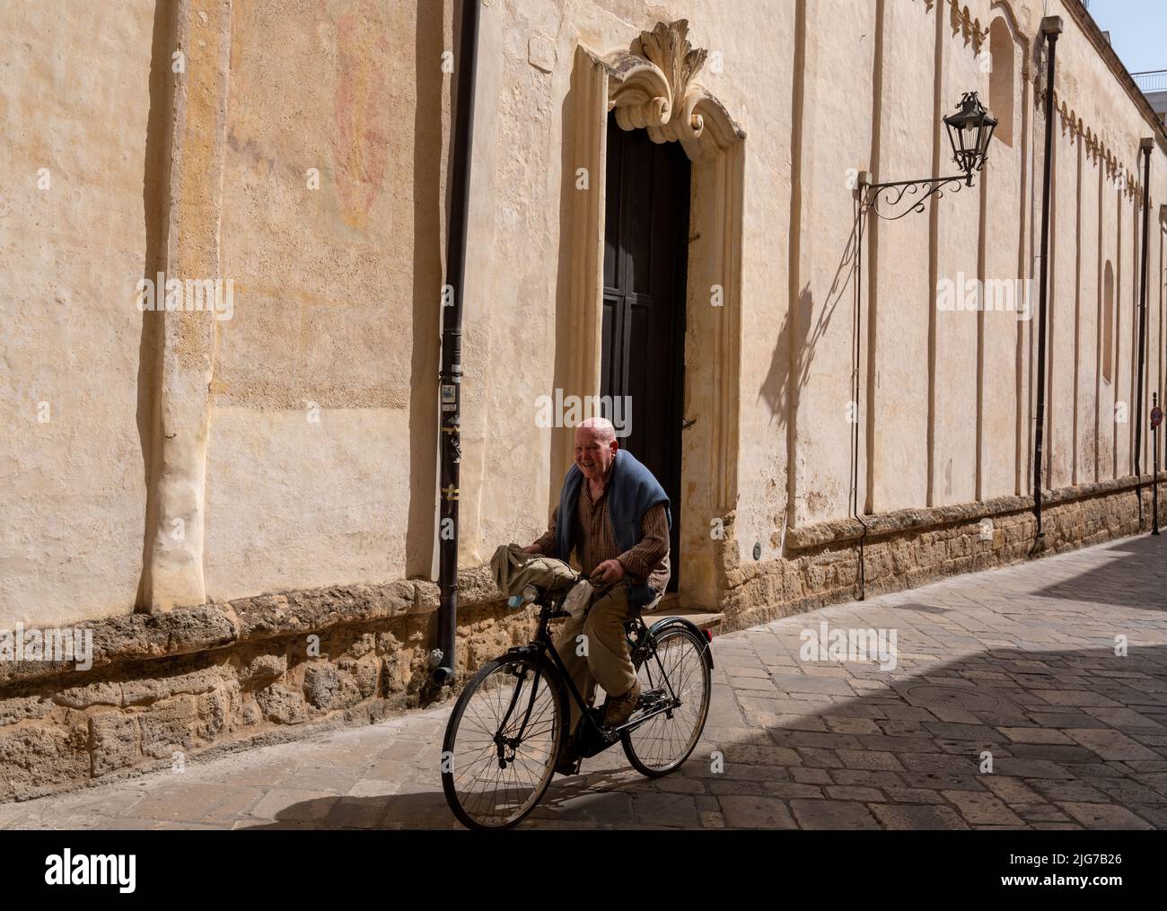 Ein älterer Mann fährt an einem heißen Sommertag mit dem Fahrrad durch die kopfsteingepflasterten Straßen der Altstadt von Nardo, Apulien, Italien Stockfoto