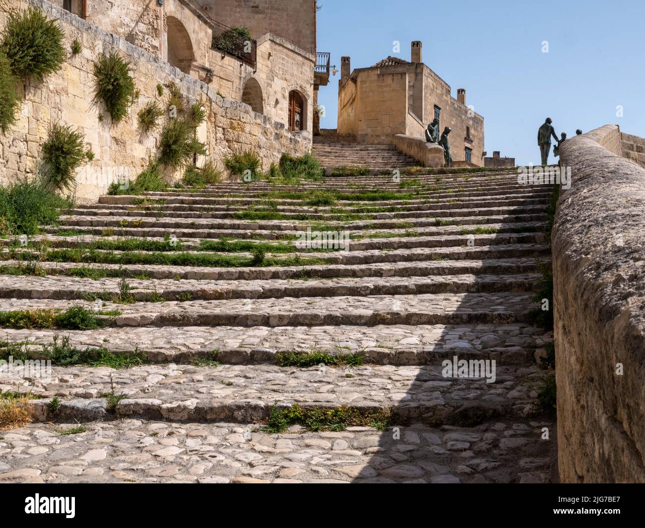 Stufen, die in der Altstadt oder in Sassi von Miera, Italien, bergauf führen, mit der Silhouette von Skulpturen menschlicher Formen an der Spitze der Treppe Stockfoto
