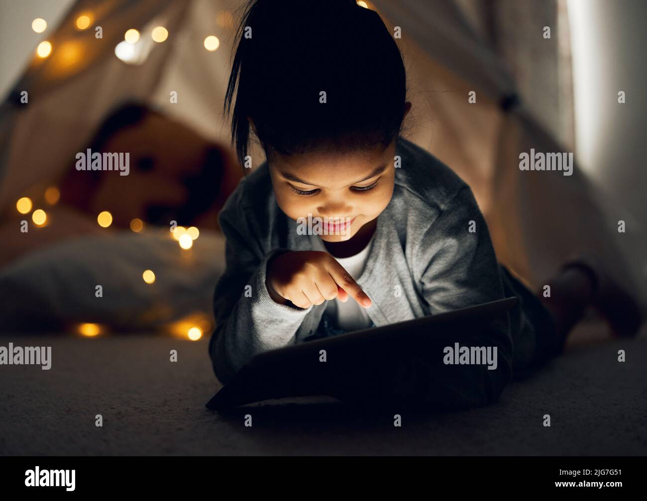 Was sollte ich als Nächstes sehen. Aufnahme eines kleinen Mädchens mit einem digitalen Tablet spät in der Nacht zu Hause. Stockfoto