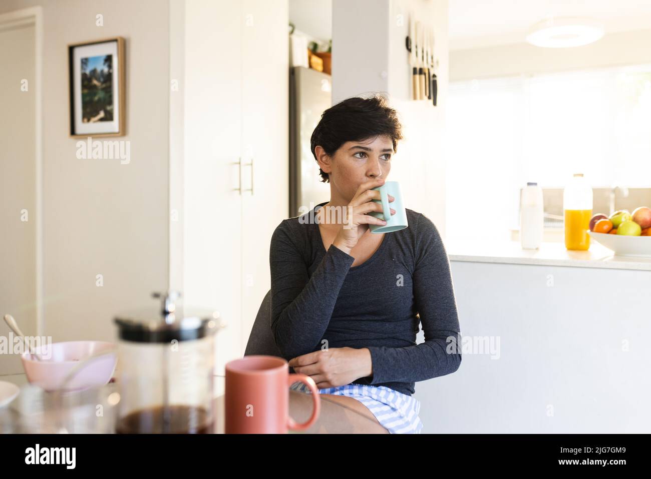Kaukasische Frau mittleren Erwachsenen mit kurzen Haaren wegschauen und Kaffee trinken, während zu Hause sitzen Stockfoto