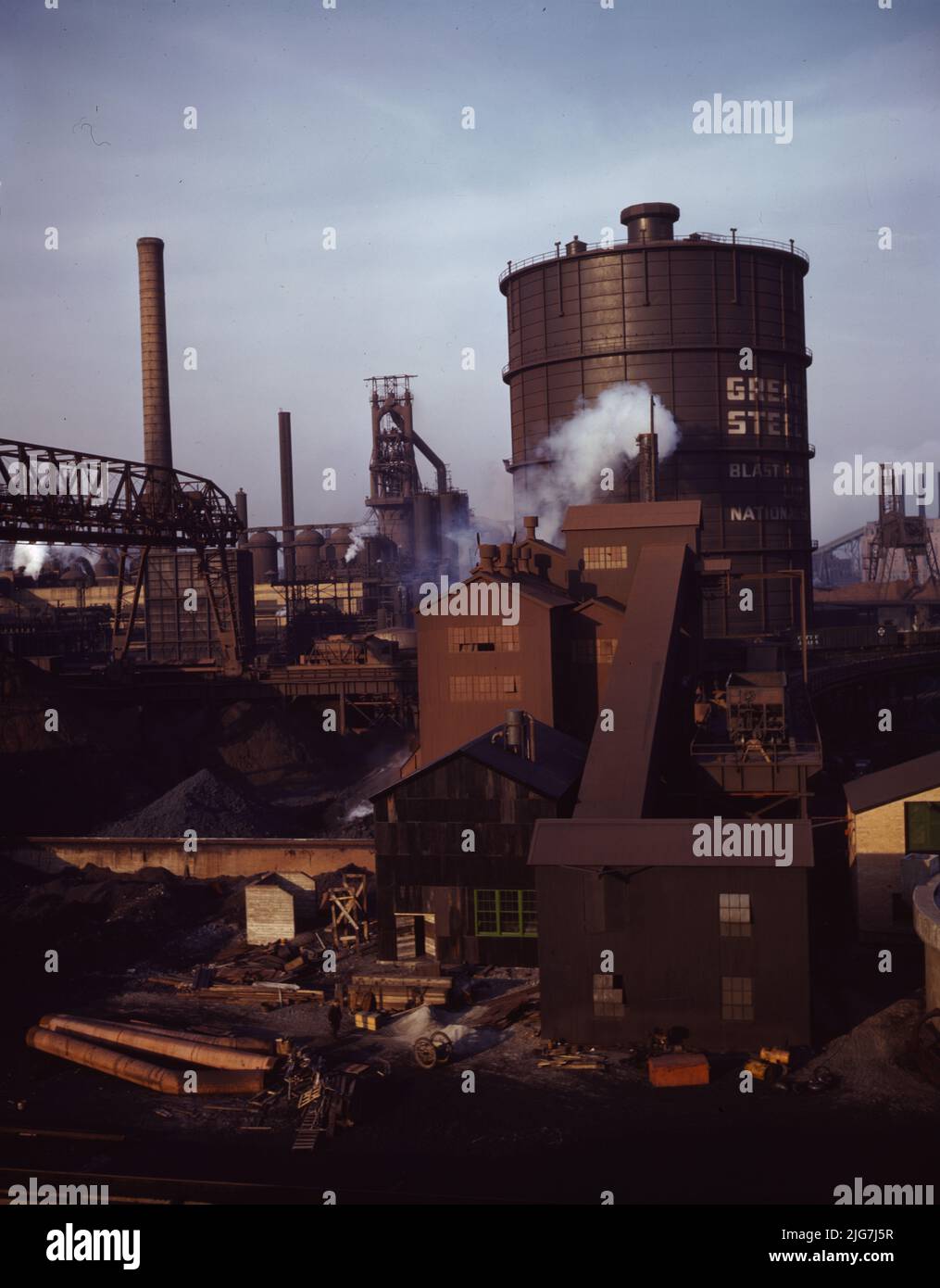 Hanna Furnaces of the Great Lakes Steel Corporation, Detroit, Michigan. Gesamtansicht eines Tanks, der Gas aus dem Koksofen speichert. In einem quadratischen Gebäude und einer Erweiterung im mittleren Erdboden wird Kohle einem Zuführband zugeführt und dann auf einen Lagerplatz auf dem Koksofen übertragen. Die Kohle wird dann in drei umgedrehte flaschenartige Behälter abgeworfen und von dort direkt in die Koksofen eingespeist. Stockfoto