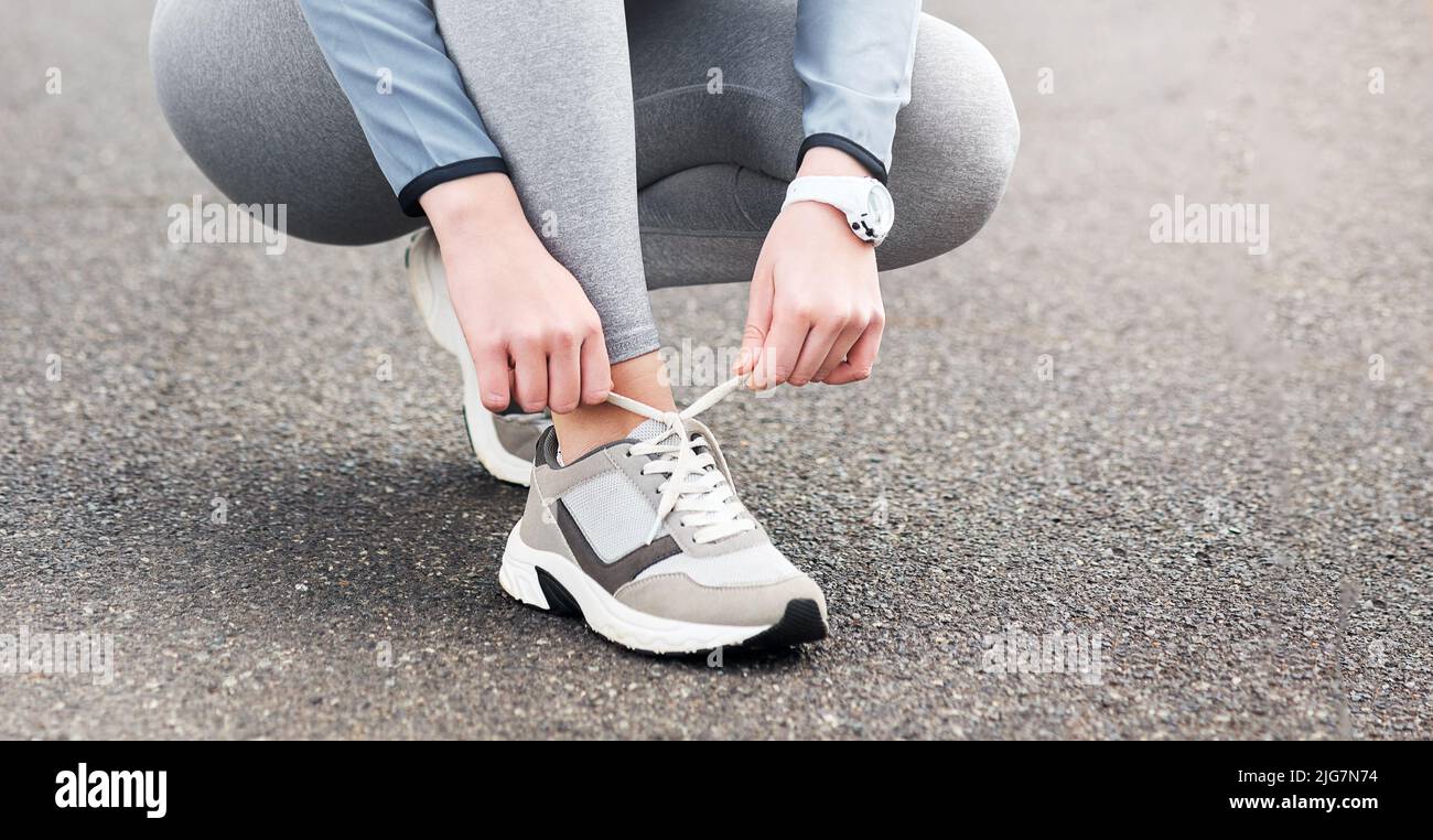 Gute Schuhe machen mich zu einem besseren Läufer. Eine kurze Aufnahme einer Frau, die ihre Schnürsenkel festbindet, während sie auf einer Straße unterwegs ist. Stockfoto