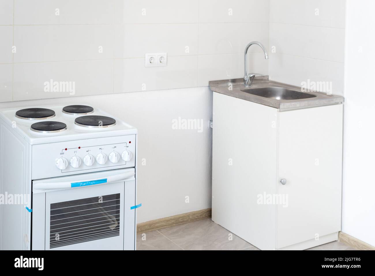 Edelstahlwaschbecken und Elektroherd in einer leeren Küche. Neues Haus. Stockfoto