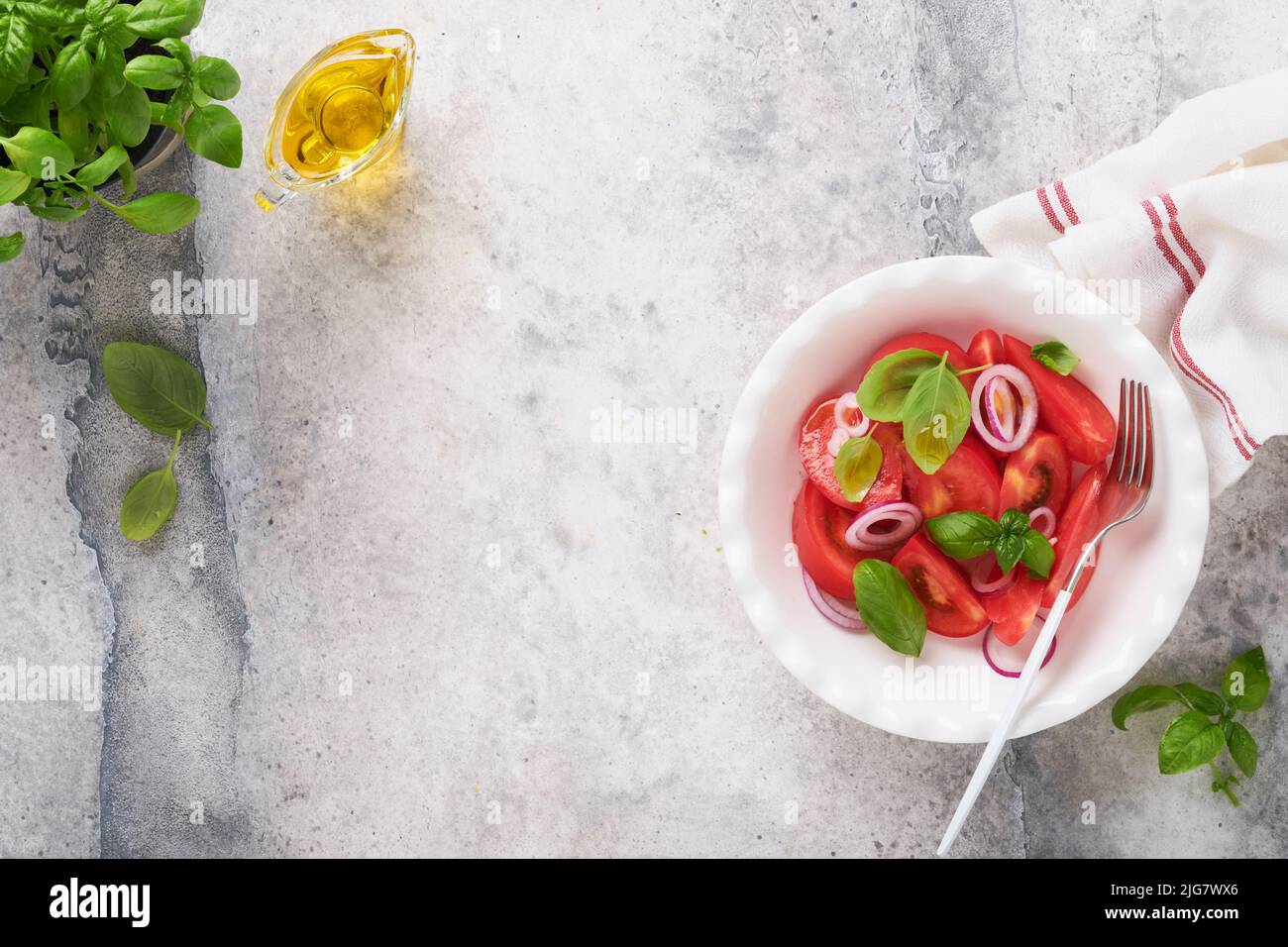 Frischer Tomaten-Salat mit Basilikumblättern, Olivenöl und Zwiebel in einer weißen Schüssel auf hellem Hintergrund. Traditionelle italienische oder mediterrane Ernährung. Top Vie Stockfoto