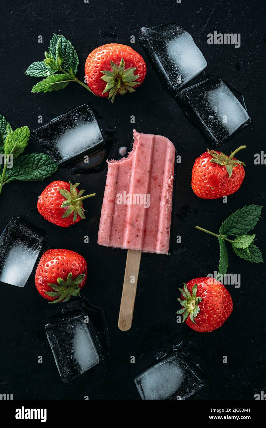 Hausgemachte Erdbeerpopsicles mit Früchten und Eiswürfeln auf dunklem Grund Stockfoto