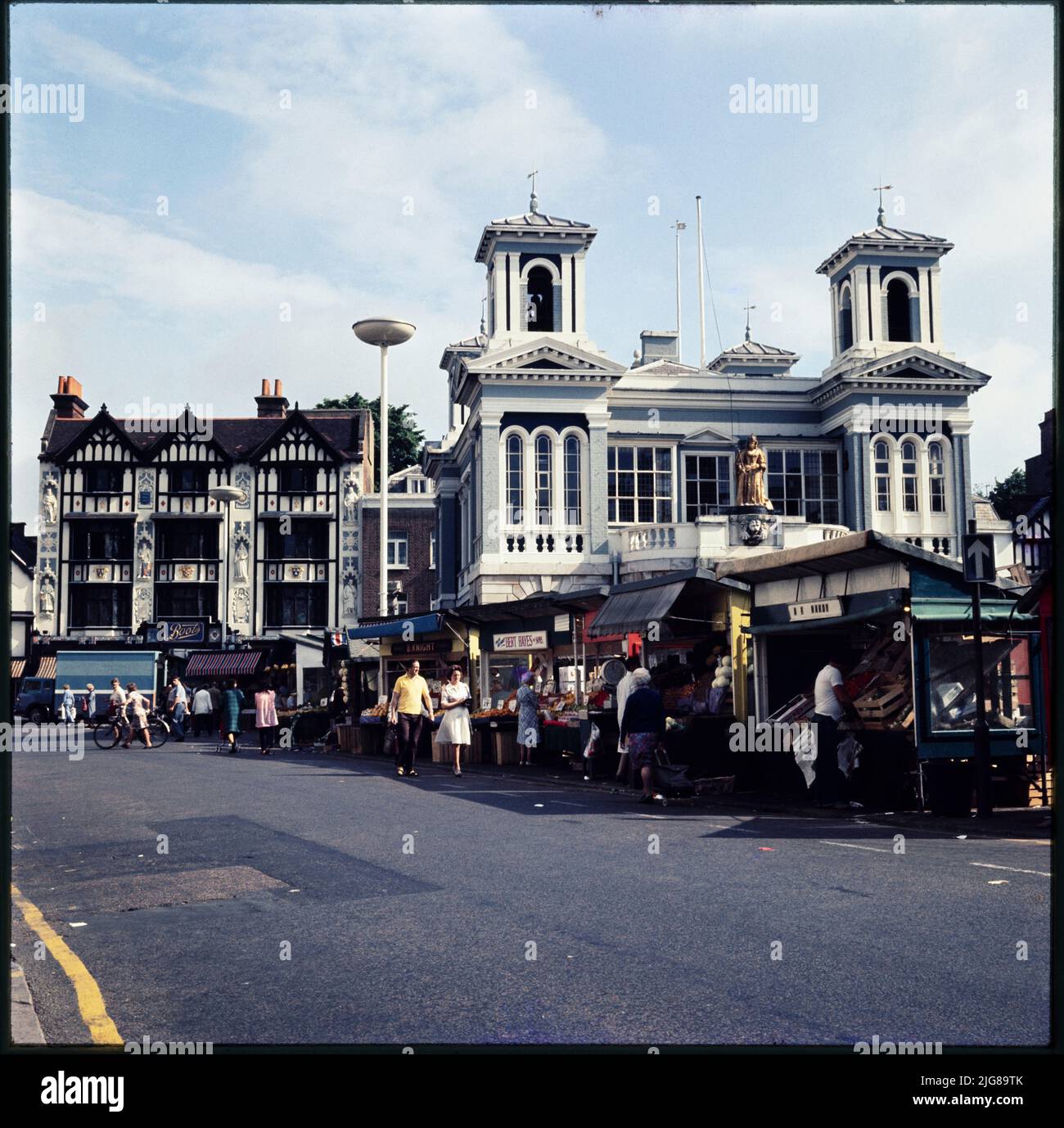 Market Place, Kingston-upon-Thames, Greater London, Authority, 1970s-1990s. Der Market Place in Kingston-upon-Thames mit Marktständen vor dem Market House und Boots, der Apotheke, im 15-16 Market Place darüber hinaus. Der Boots-Shop am 15-16 Market Place wurde 1909 im jakobean-revival-Stil nach einem Entwurf von Michael Vyne Treleaven erbaut. Die Statuen an der Fassade und die Glasmalerei erinnern an die Krönung der sächsischen Könige in Kingston. Stockfoto