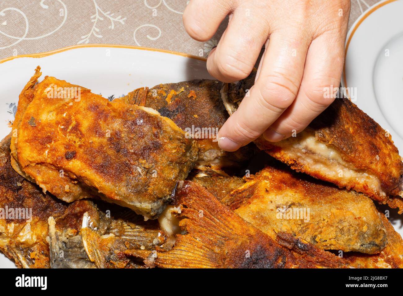Beim Abendessen greift die Hand eines Mannes nach einem Stück gebratenem Karpfenfisch. Köstliche kalorienreiche Lebensmittel. Stockfoto