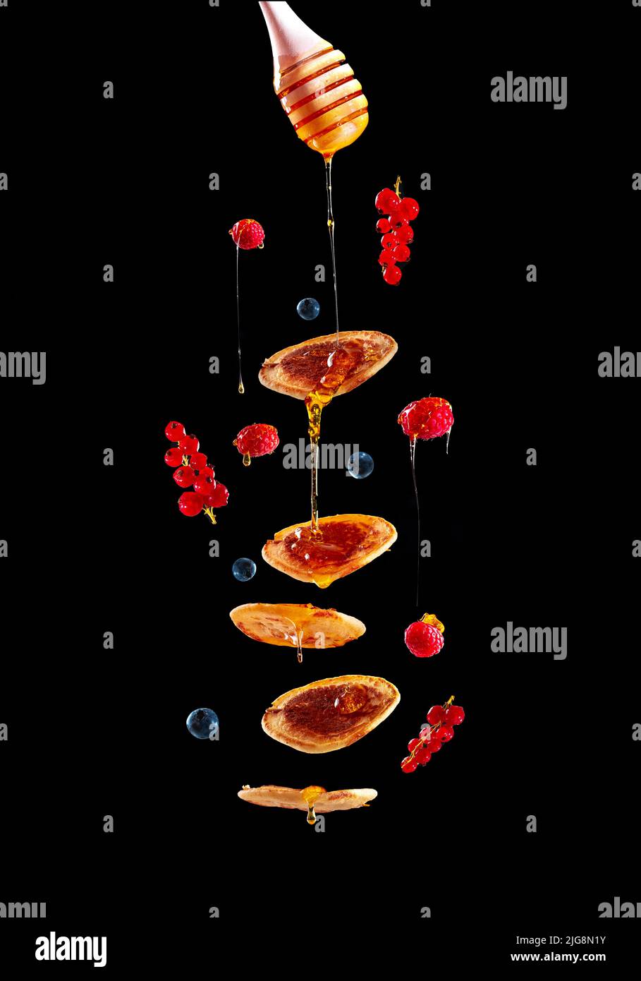 Pfannkuchen mit Obst und Honig auf schwarzem Hintergrund, der in der Luft fliegt. Mini-Pfannkuchen mit Heidelbeeren und Himbeeren. Amerikanisches Frühstück im Dunkeln Stockfoto