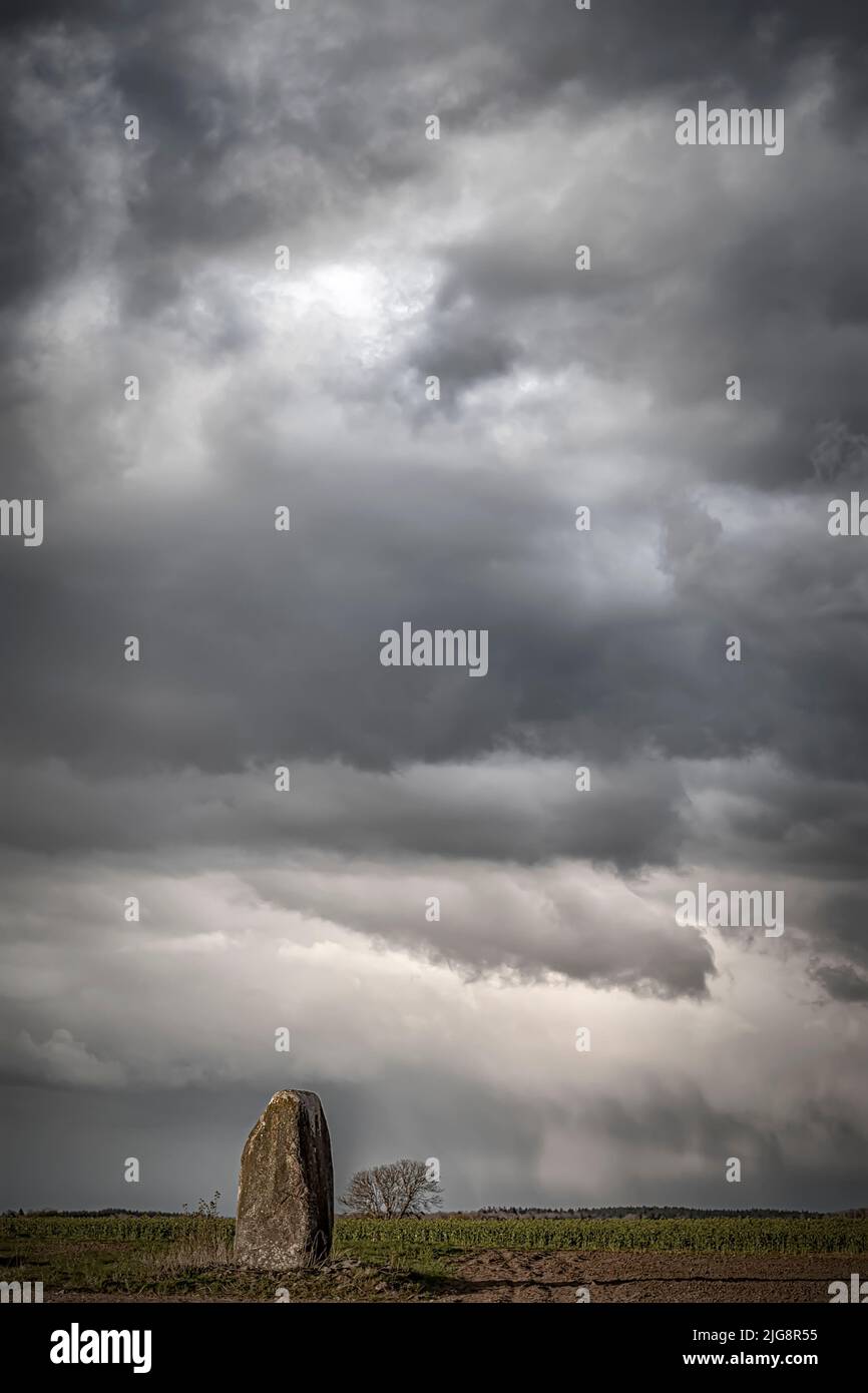 Ein einziger Stein, der in der schwedischen Landschaft vor einem dramatischen bewölkten Himmel steht Stockfoto