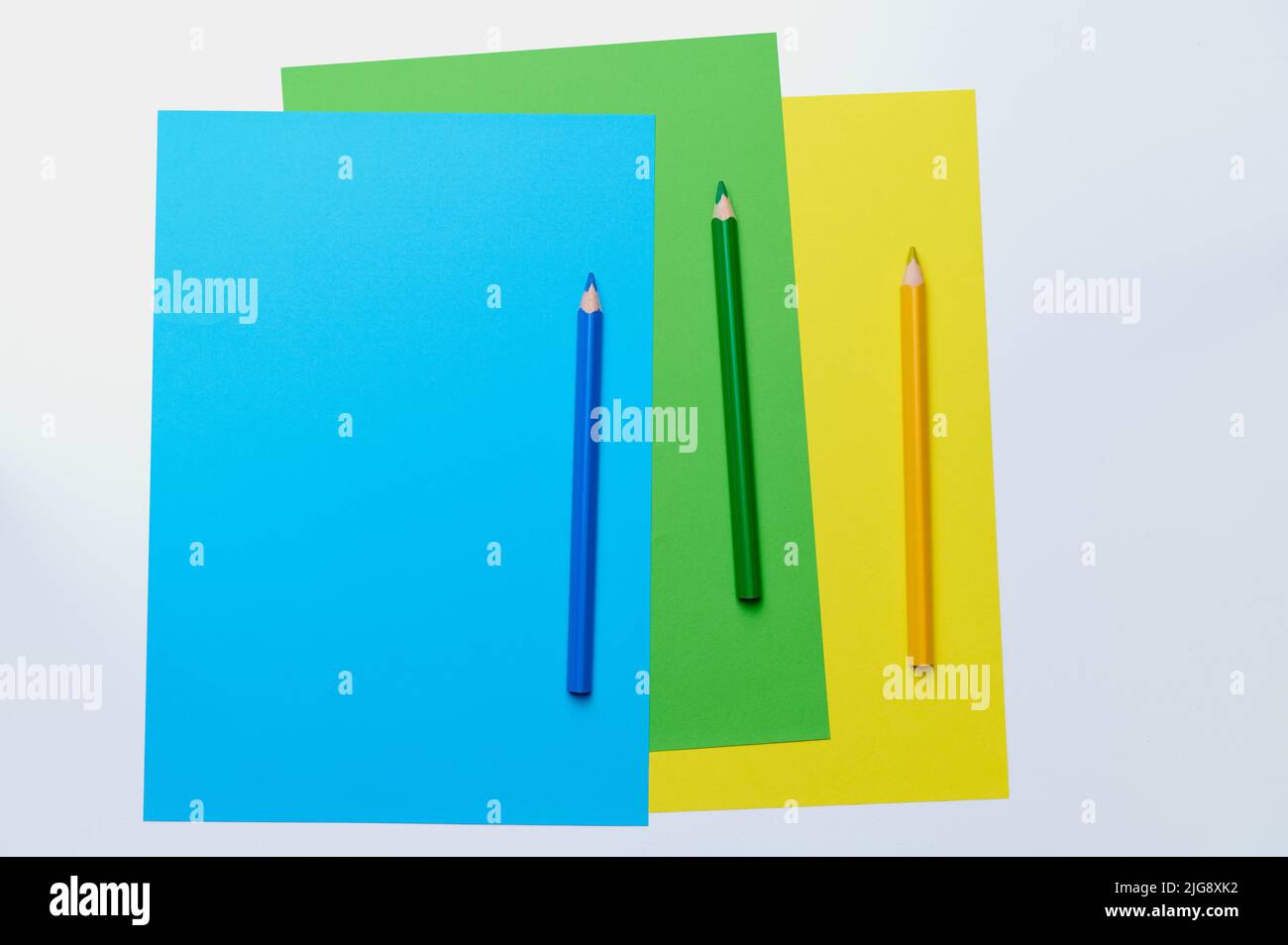 Drei Buntstifte auf blauem, grünem und gelbem Papier Stockfoto