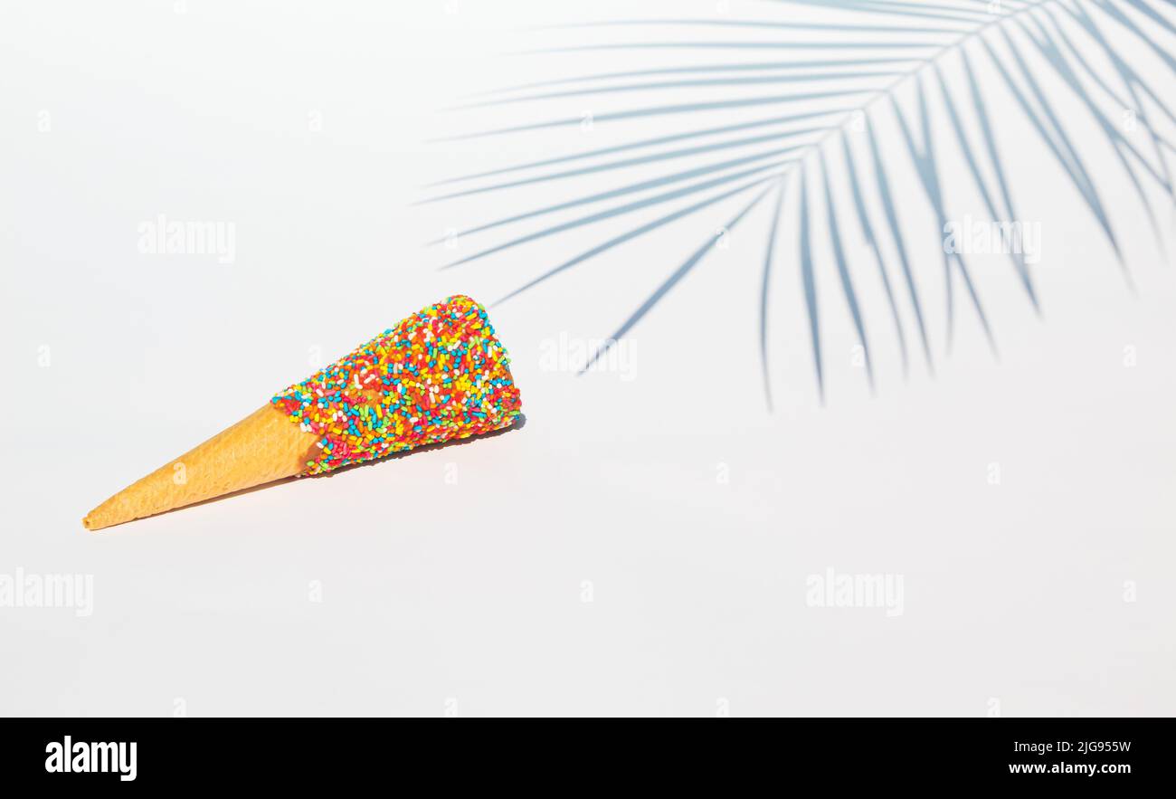 Palmenblatt Schatten und bunte Eis Kegel mit Streuseln auf weißem Hintergrund. Tropisches Sommerkonzept. Stockfoto