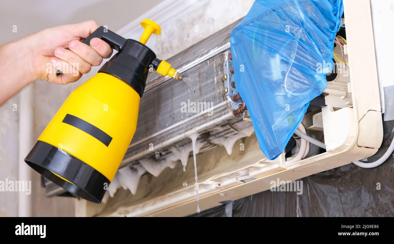 Ein Mann wäscht einen speziellen Schaum ab, um Klimaanlagen mit einem Wasserstrahl unter Druck zu reinigen. Wartung des geteilten Systems. Stockfoto