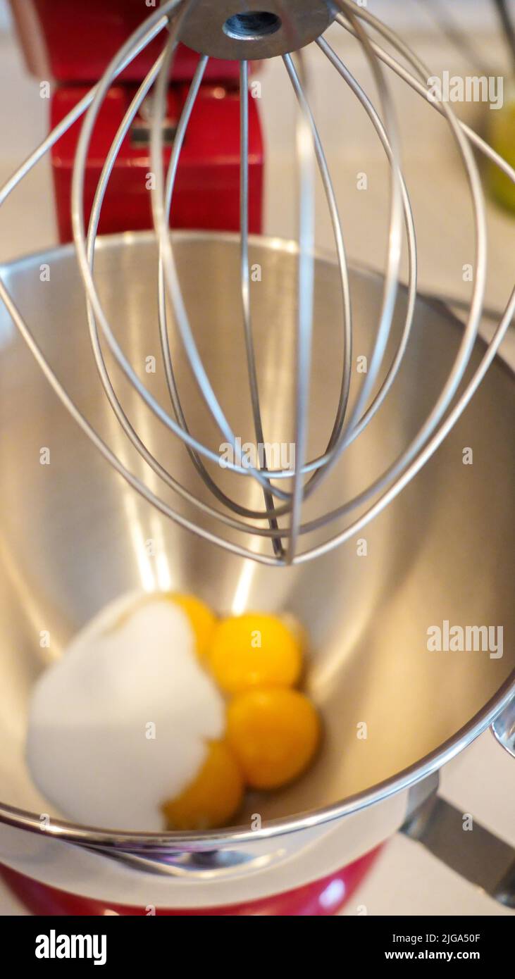 Nahaufnahme gelbe Eier in einer Metallmixer-Schüssel. Roter Standmixer mit weißem Hintergrund. Stockfoto