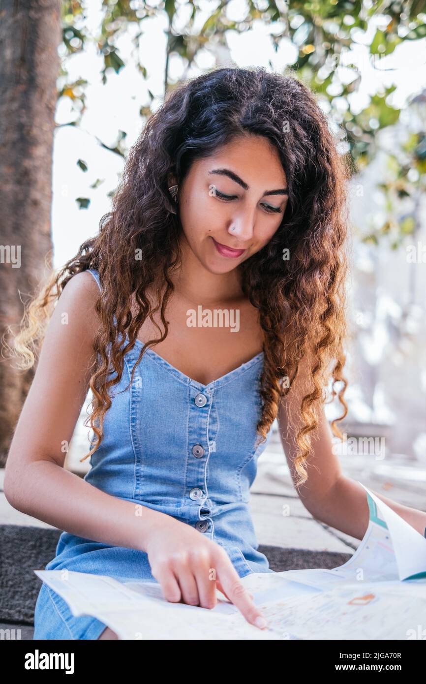 Indische Touristenin, die Papierkarte überprüft und an einem sonnigen Tag auf der Straße der Altstadt auf einer Treppe sitzt Stockfoto