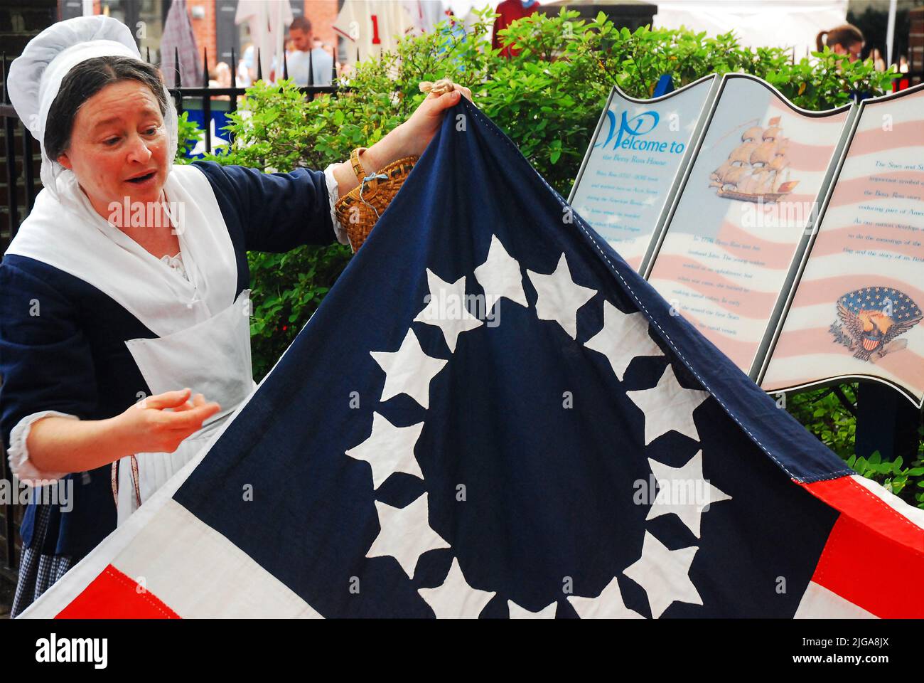 Ein Betsy Ross Reenactor entfaltet eine frühe amerikanische Flagge und zeigt, wie die Näherinnen die Flagge in Philadelphia entworfen und geschaffen haben Stockfoto