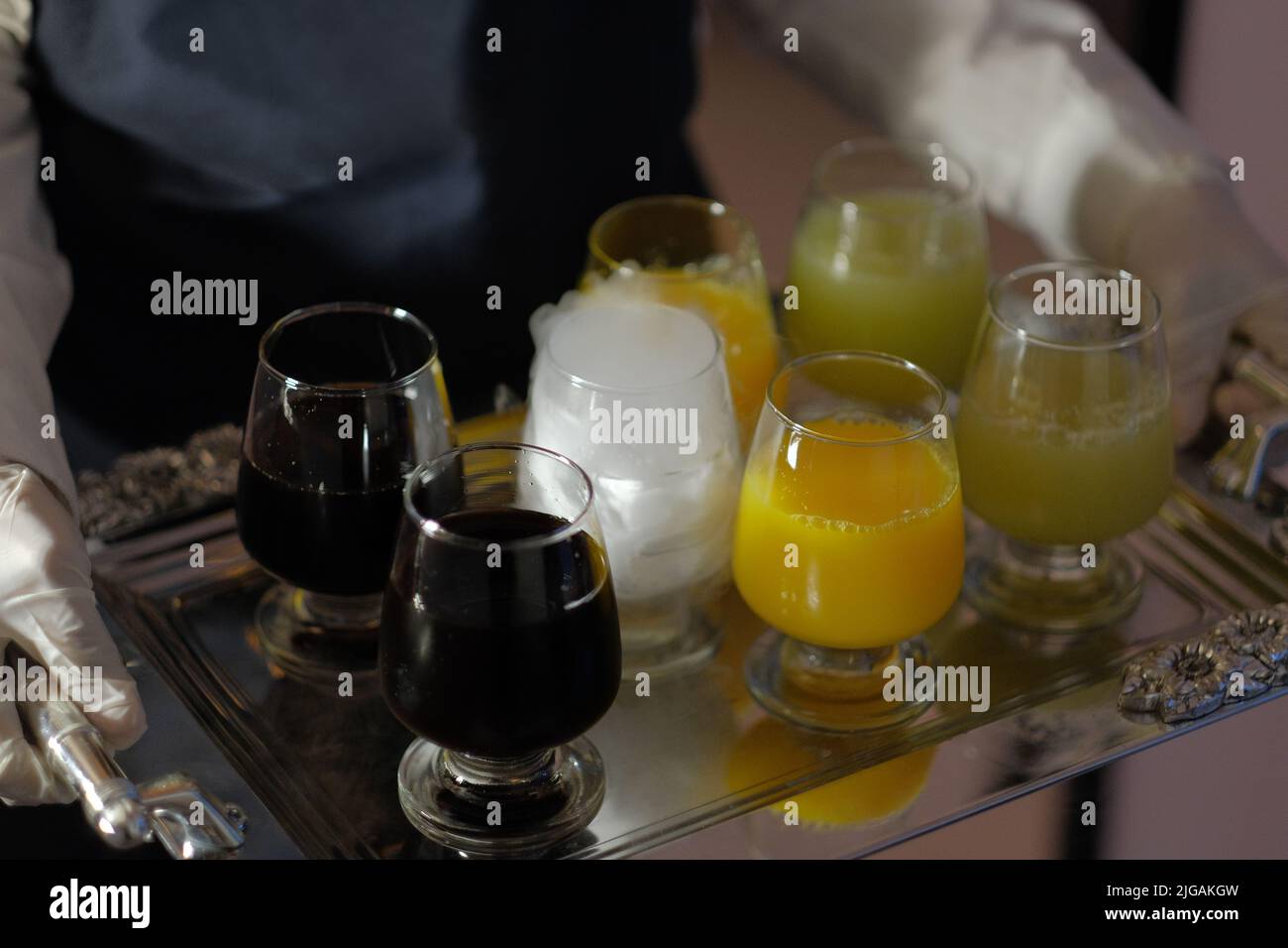 Nahaufnahme eines silbernen, glänzenden Tabletts mit verschiedenen kalten Getränken, die auf einer Party serviert werden. Ein Glas mit Trockeneis erzeugt weißen Rauch für das visuelle Interesse. Stockfoto