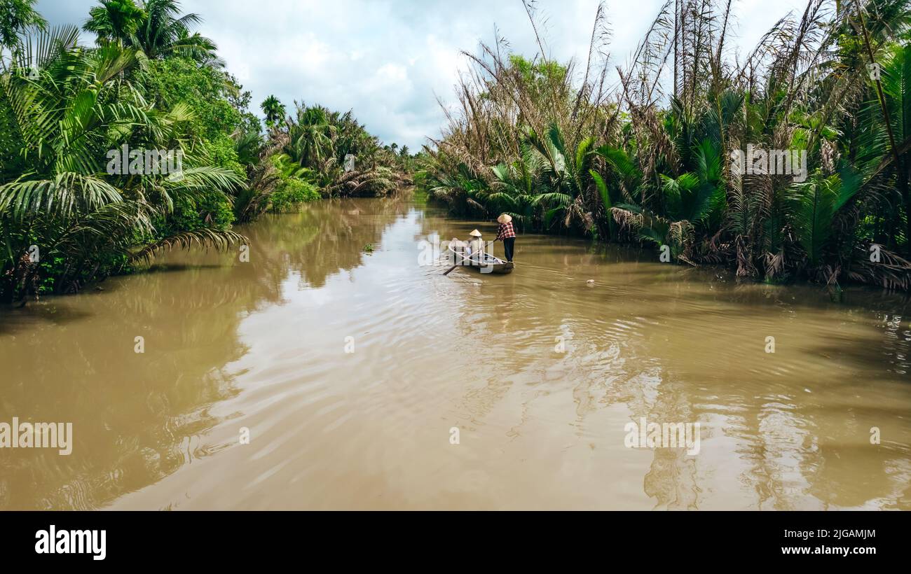 Tourist auf Sampan Bootstour in den Mekong Flusskanälen mit Frau, die in vietnamesischem Hut paddelt Stockfoto