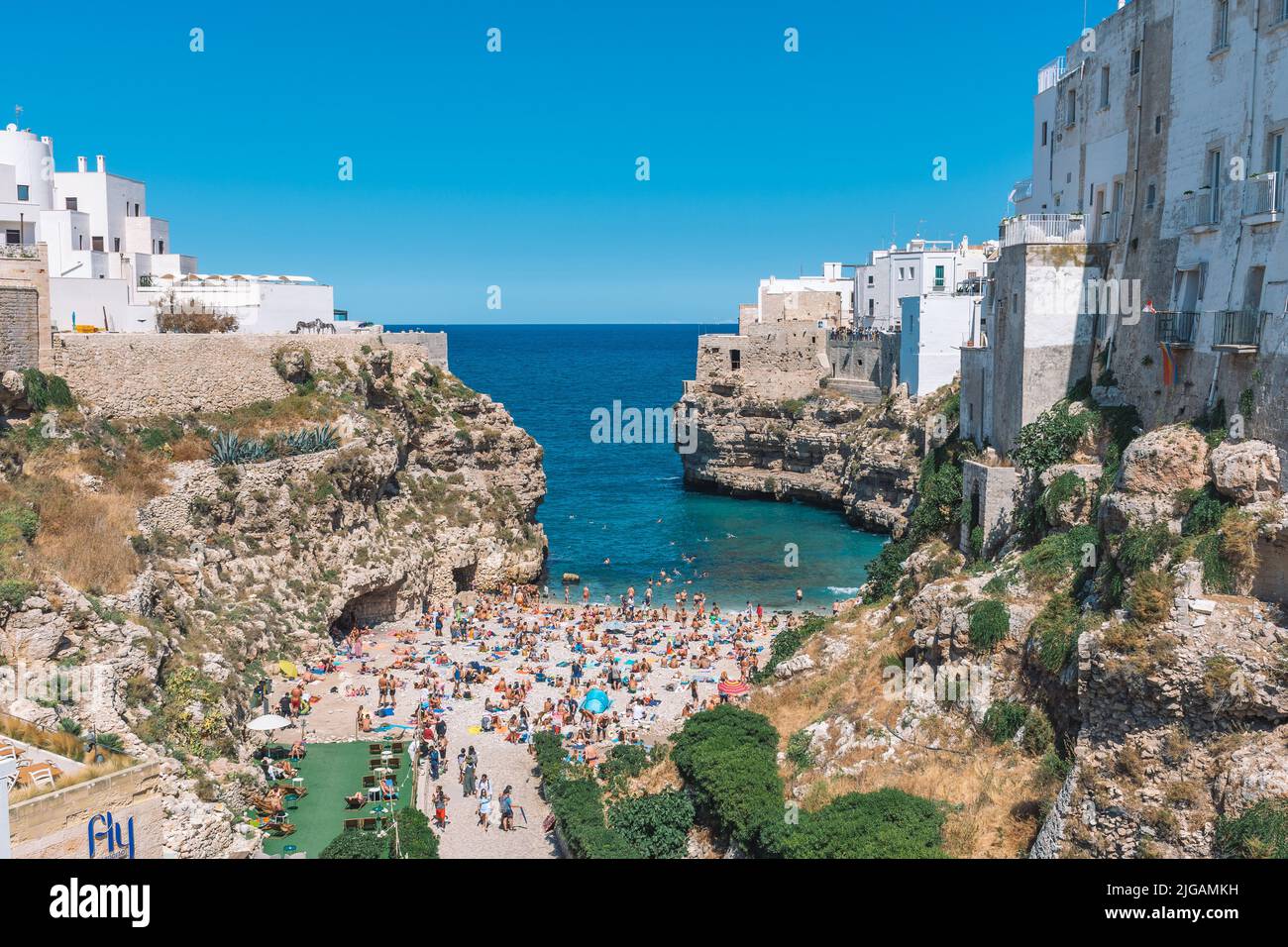 Schöne Luftaufnahme von Polignano a Mare mit weißen Steinhäusern, Klippen, Strand, blaues Meer und Touristen, Badegäste, umgeben von mediterraner Natur Stockfoto