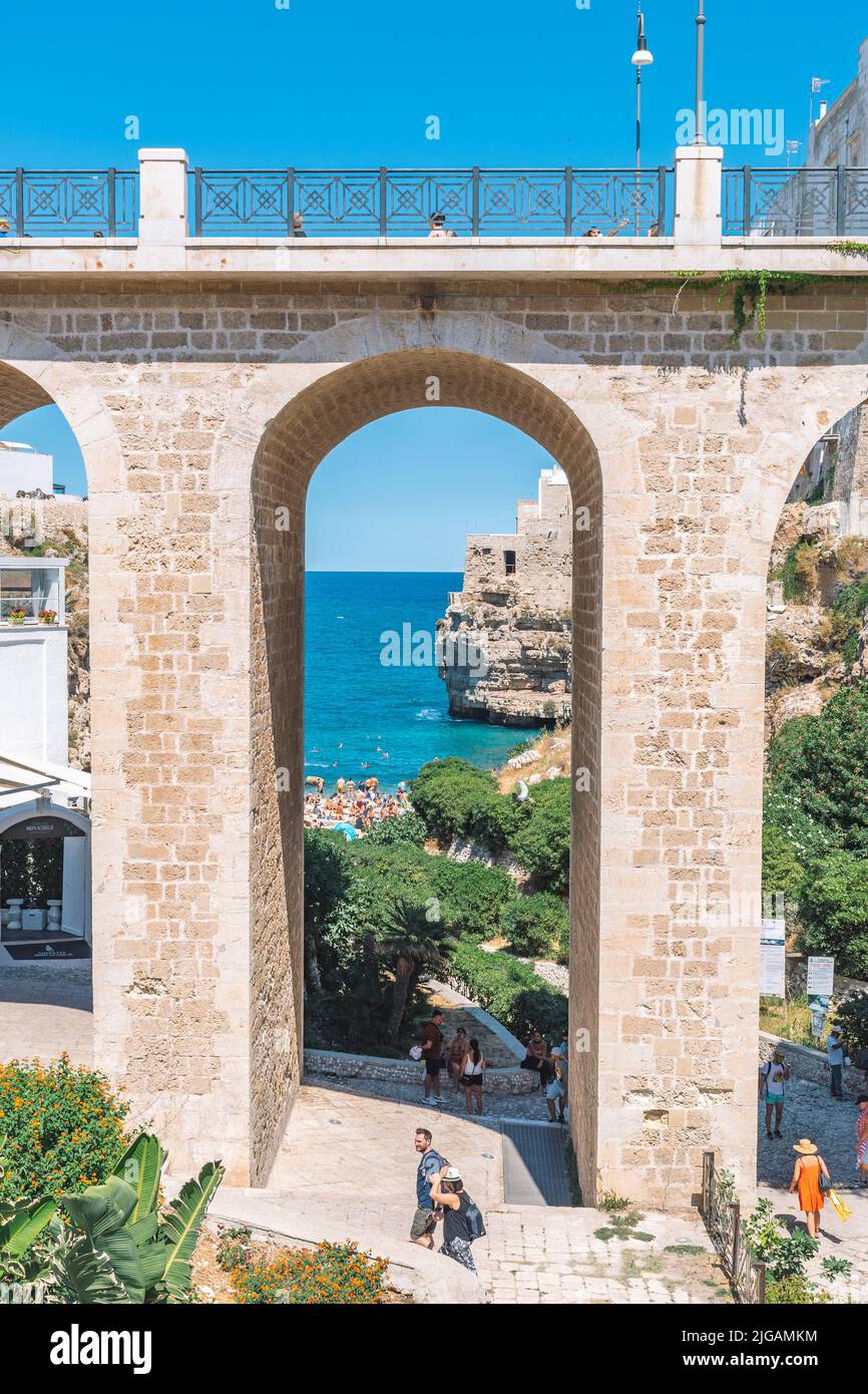 Schöne Aussicht auf Polignano a Mare mit weißen Steinhäusern, Klippen, Strand, blaues Meer und Touristen, Badegäste, umgeben von mediterraner Natur Stockfoto