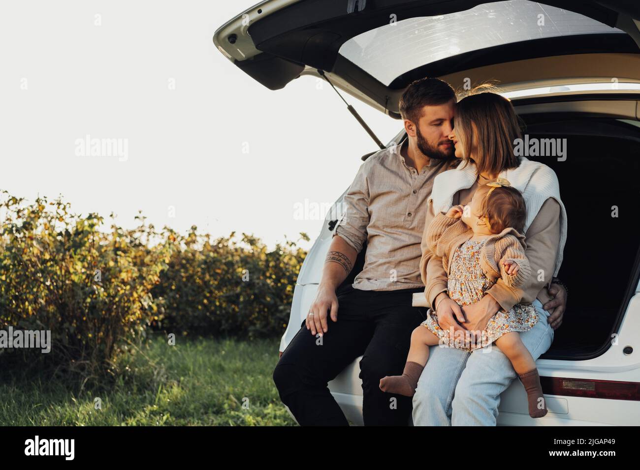 Junge kaukasische Familie sitzt im Kofferraum des SUV-Autos, Mama und Papa mit Baby-Tochter Spaß am Wochenende im Freien Stockfoto