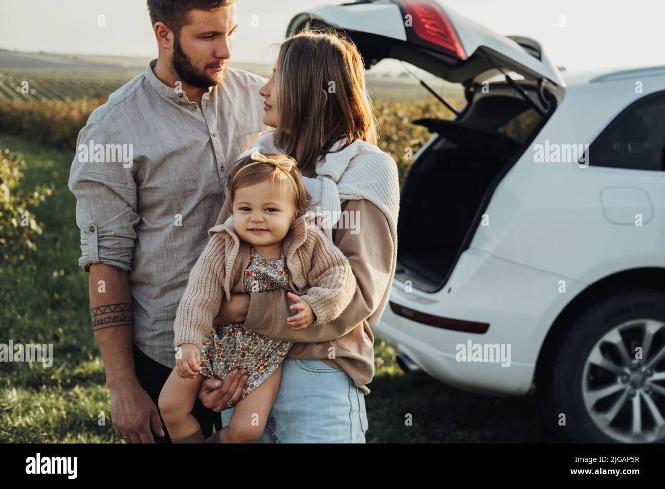 Junge kaukasische Familie genießen Roadtrip, Mutter und Vater mit kleinen Tochter im Freien mit SUV-Auto auf dem Hintergrund Stockfoto
