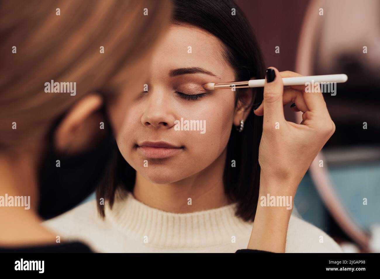 Nahaufnahme Make-up-Künstlerin in Schutzmaske Arbeiten mit dem Augenlid des Kunden, Junge Frau bei der Prozedur im Schönheitssalon Stockfoto