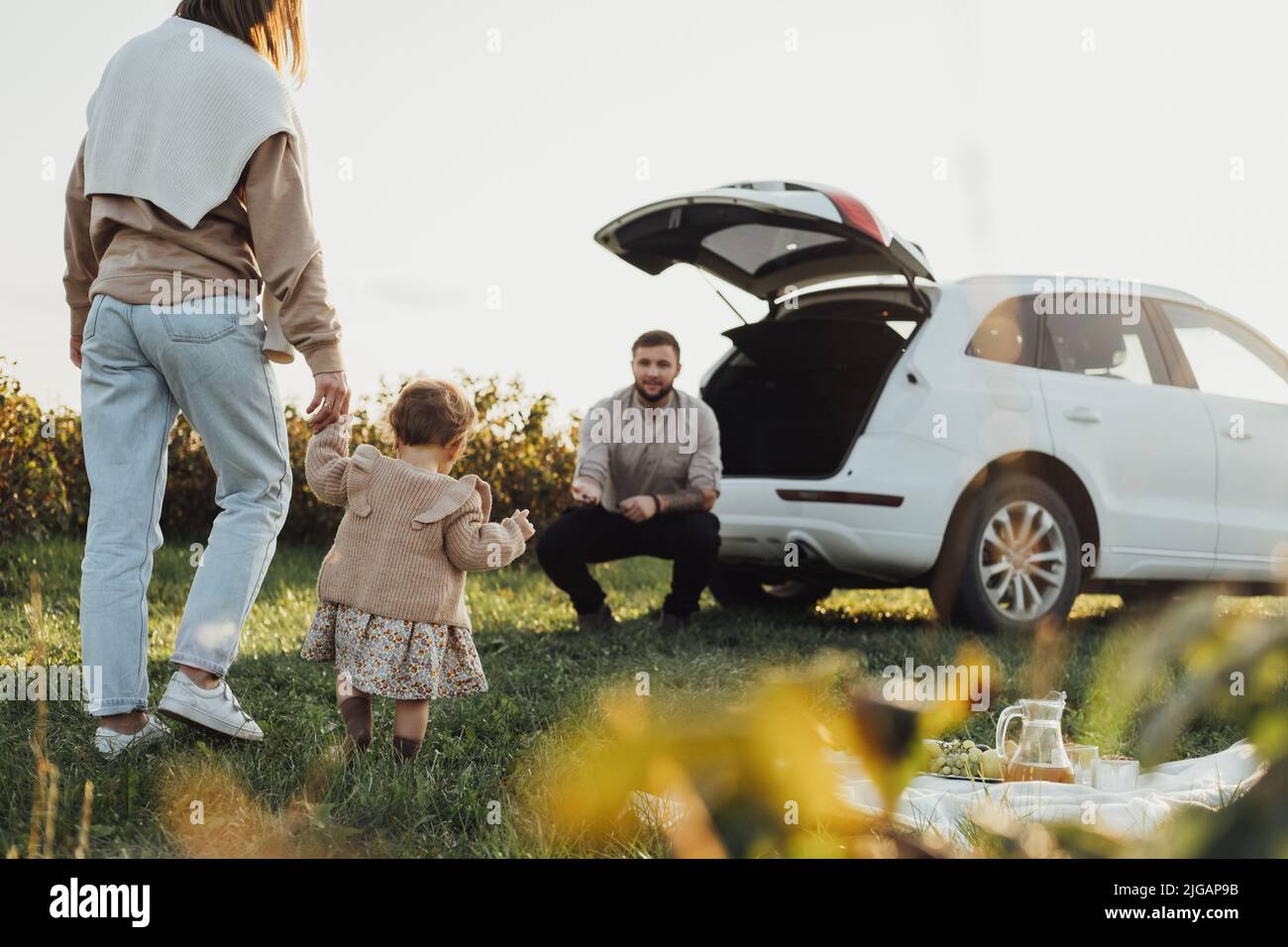 Junge Familie genießt Roadtrip, Mutter und Vater mit kleiner Tochter im Freien mit Picknick mit SUV-Auto auf dem Hintergrund Stockfoto
