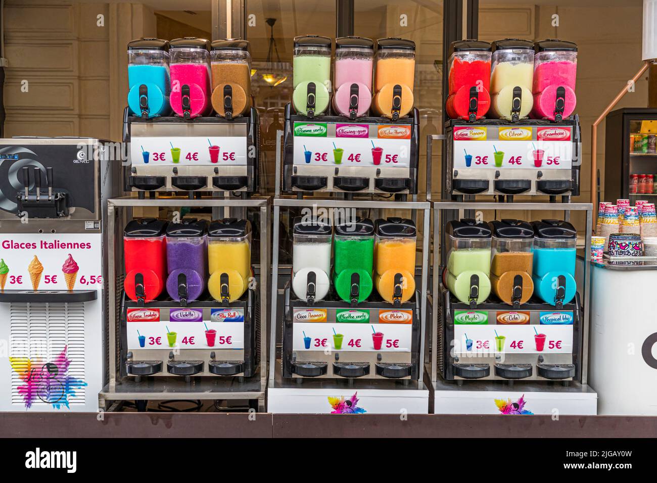 Weiche Eiscreme in hellen, lebendigen Farben füllt sechs Spenderautomaten an einem Straßenstand in Montpellier, Frankreich. Die Preistafeln listen 3 bis 5 Euro je nach Größe auf, während klassische italienische Eiswaffeln zusätzlich für 3 bis 6,50 Euro beworben werden. Stockfoto