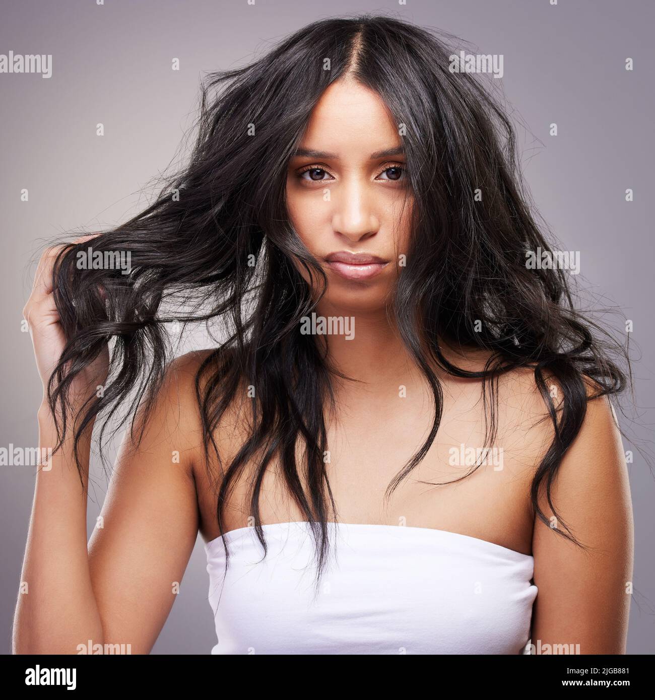 Ich bin offiziell im Krieg mit meinen Haaren. Eine attraktive junge Frau, die allein im Studio steht und sich frustriert fühlt, während sie auf ihre Haare schaut. Stockfoto