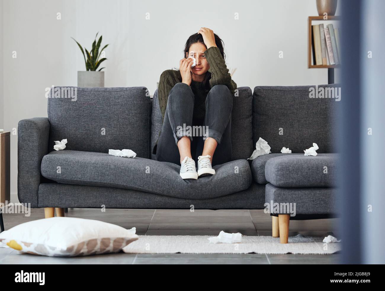 Ich bin viel zu rein für diese Erde. In voller Länge eine attraktive junge Frau, die allein auf dem Sofa zu Hause sitzt und weint. Stockfoto