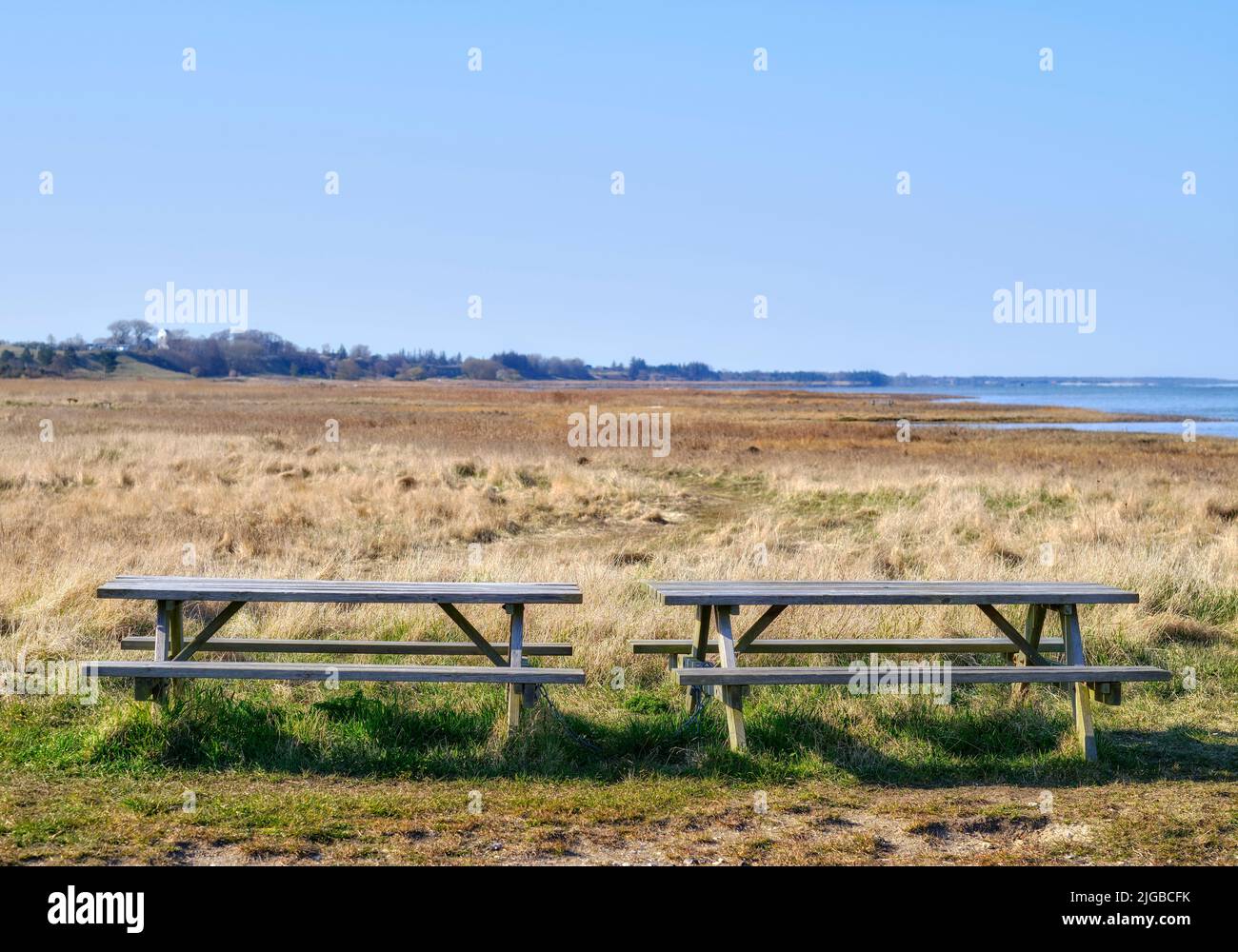 Zwei Holzbänke auf einem Feld mit Blick auf das Meer. Ein ruhiger Ort, um die Natur und die Ruhe zu genießen, die sie zu bieten hat. Finden Sie Ruhe im Grünen Stockfoto