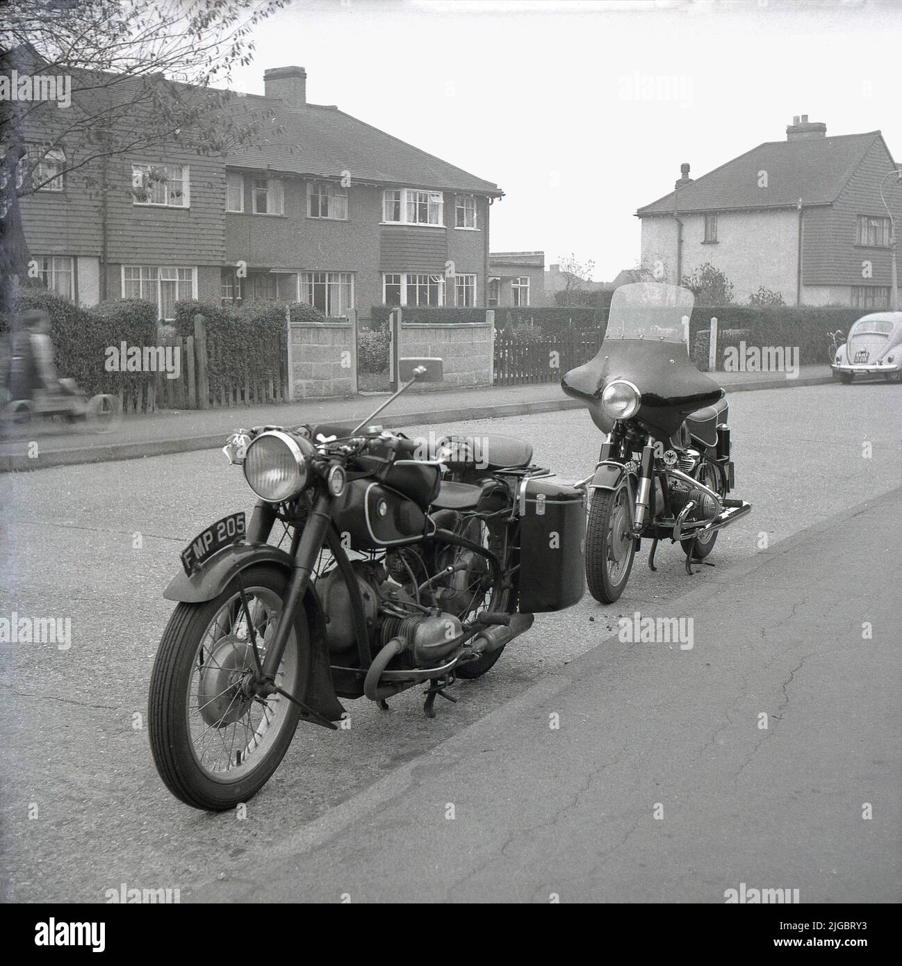 Um 1960s, historisch, zwei Motorräder der Zeit, die in einer Stadtratstraße geparkt wurden, Greater London, England, Großbritannien, ein BMW R51/3 Motorrad und dahinter ein weiteres BMW Fahrrad mit Verkleidung, möglich ein R69. Ein Junge auf einem selbstgemachten Wagen auf dem Bürgersteig gegenüber. Ein Käfer Auto ist auf der Straße geparkt. Stockfoto