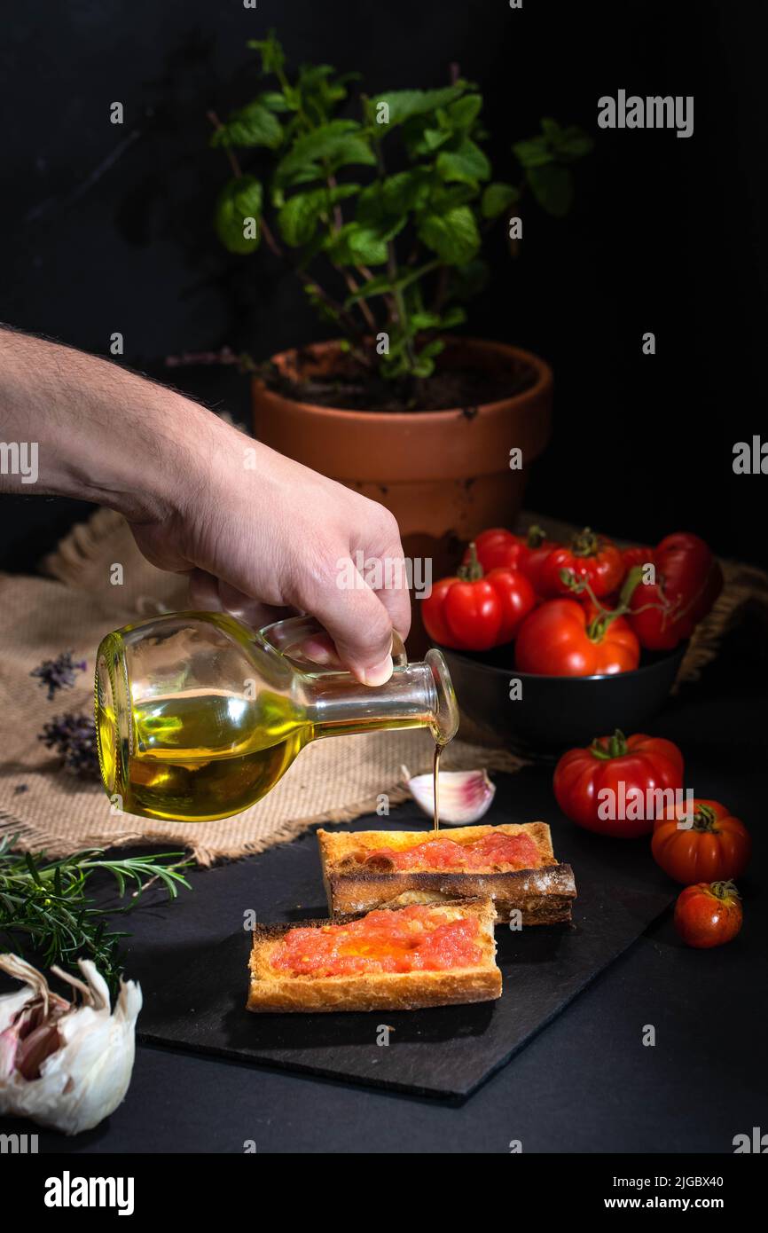 Gießen von Olivenöl auf der Oberseite der traditionellen spanischen Vorspeise - 'Pan Tomaca' (Brot mit Tomaten) geröstetes Brot mit Knoblauch gekrönt mit frisch gepressten Stockfoto