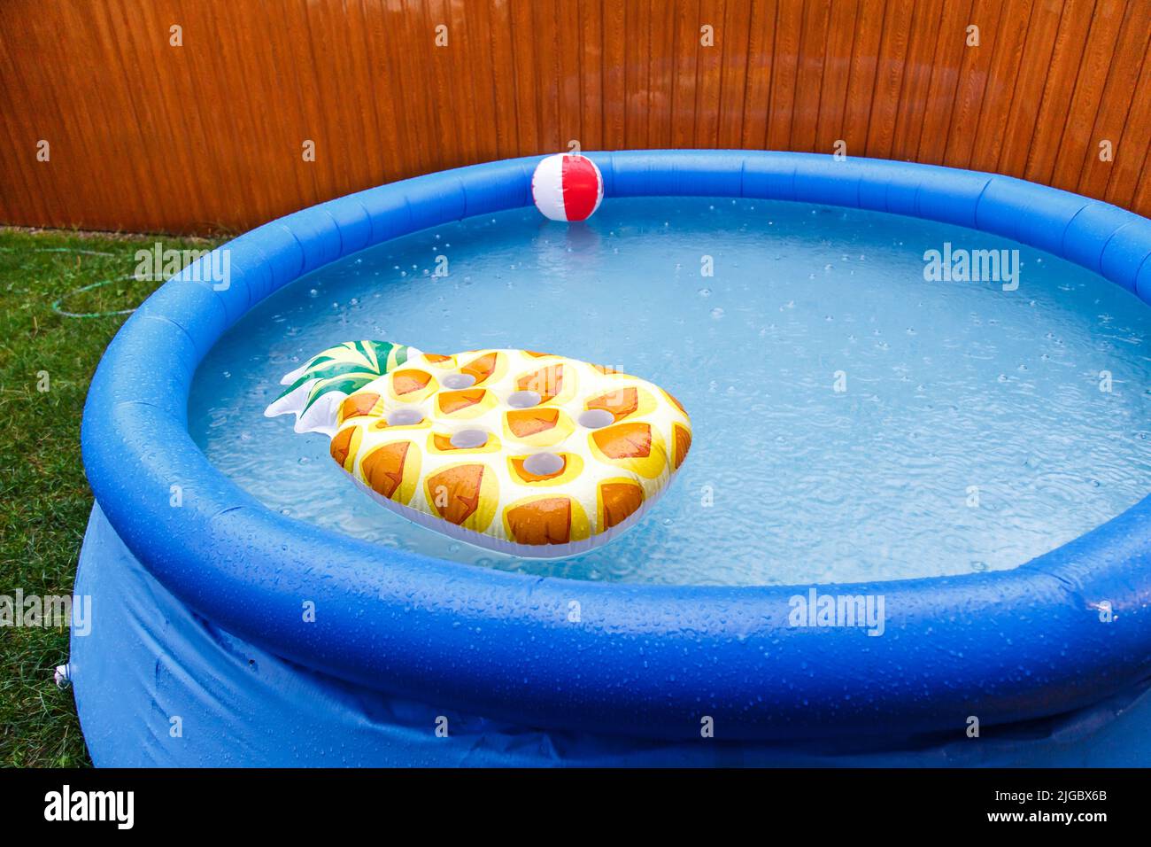 Float-Matratzen im Pool, es regnet. Blauer aufblasbarer Pool eine aufblasbare Matratze in Form einer Ananas schwebt im Pool. Stockfoto