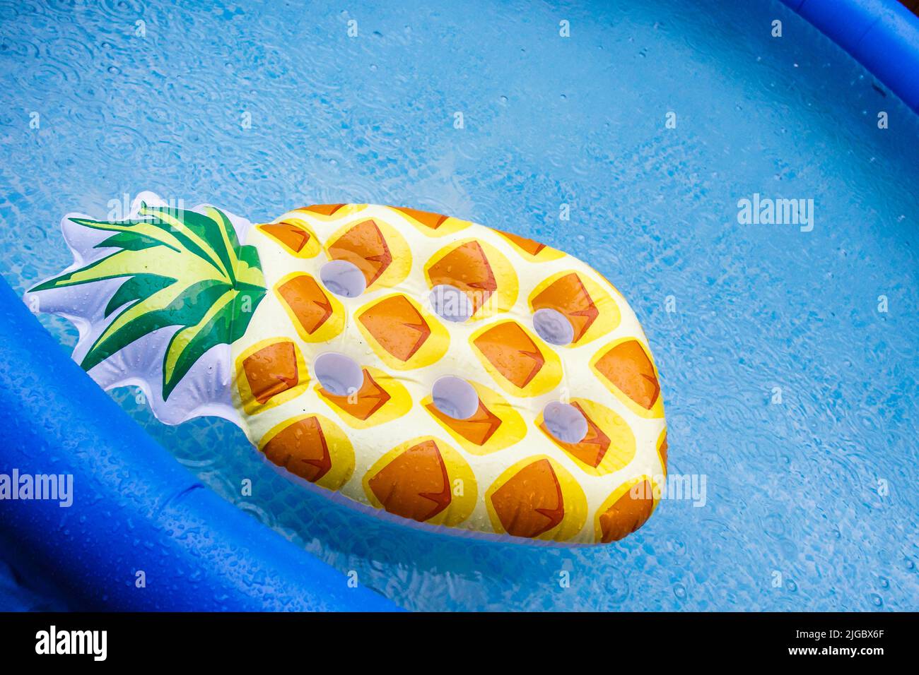 Float-Matratzen im Pool, es regnet. Blauer aufblasbarer Pool eine aufblasbare Matratze in Form einer Ananas schwebt im Pool. Stockfoto
